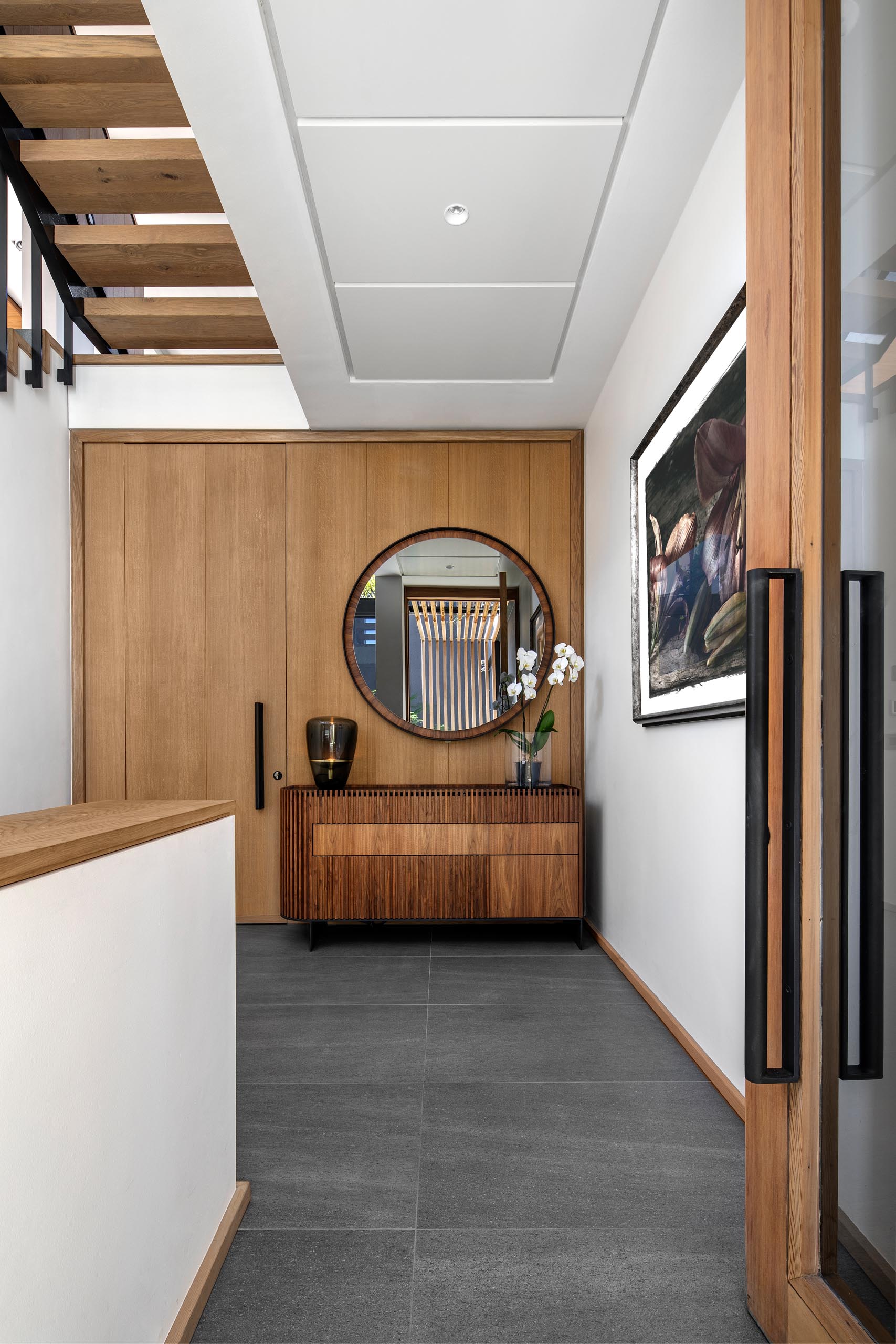 A modern entryway furnished with a wood console table, artwork, and a round mirror.