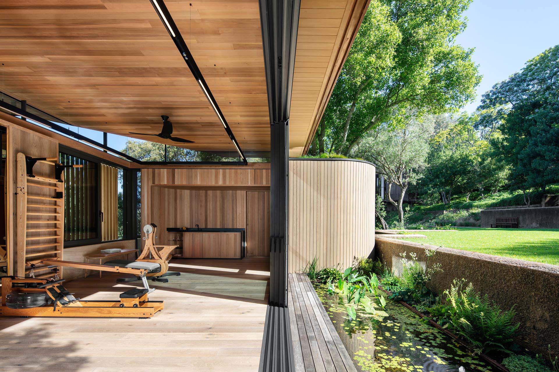 A modern home gym with glass walls that open to the outdoors.