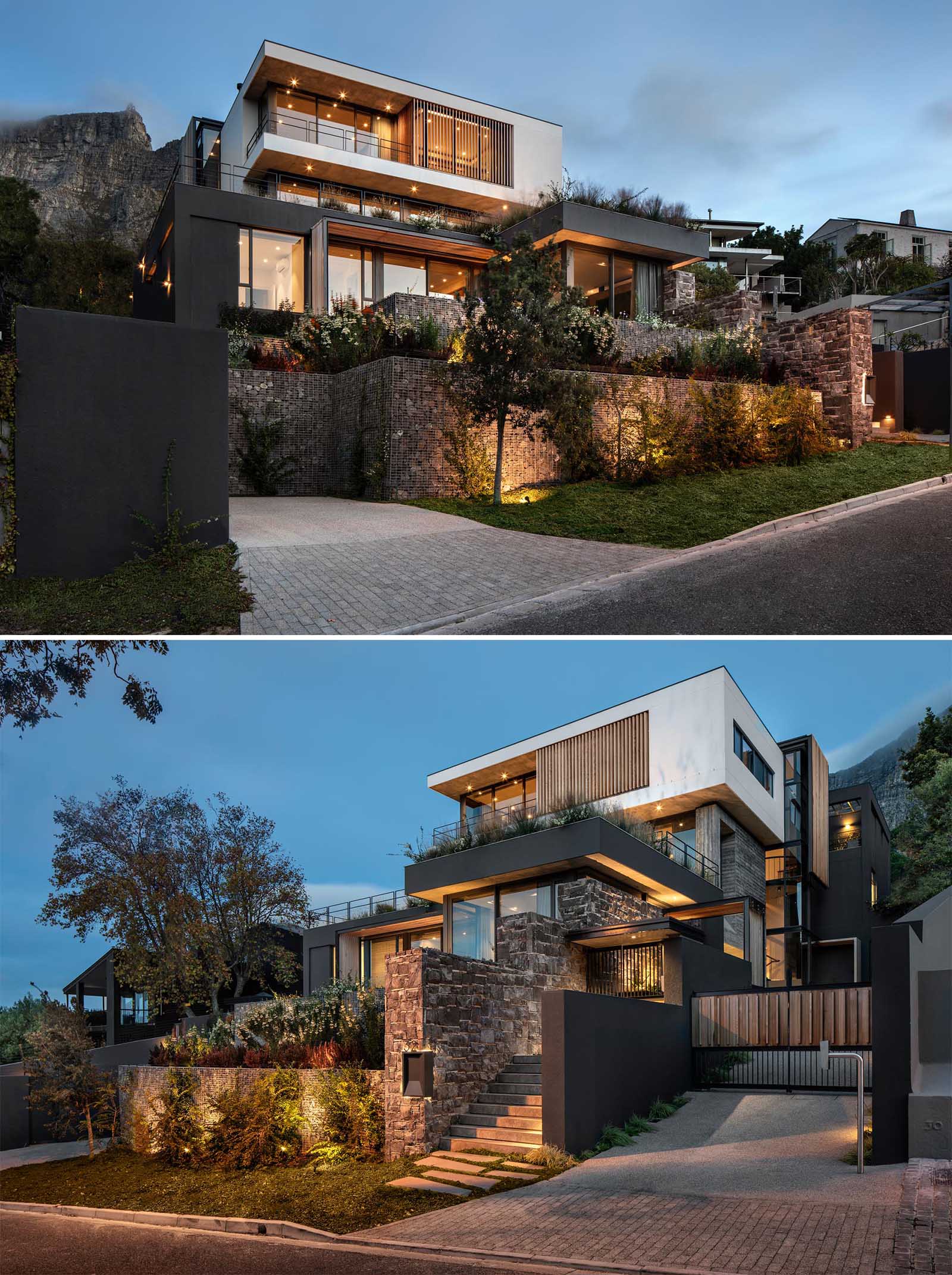 Stone and gabion walls with plants are lit up by exterior lighting at the front of this modern home, while wood slats add a natural element on the upper level of the home.