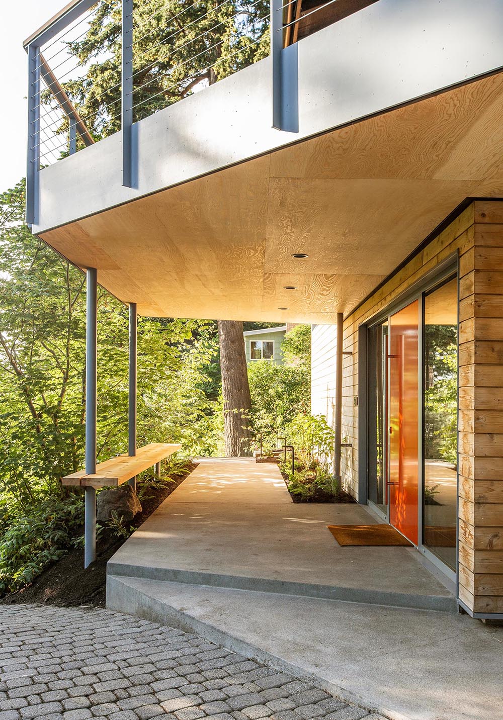 A partially covered walkway with a cedar bench leads people to the front door.