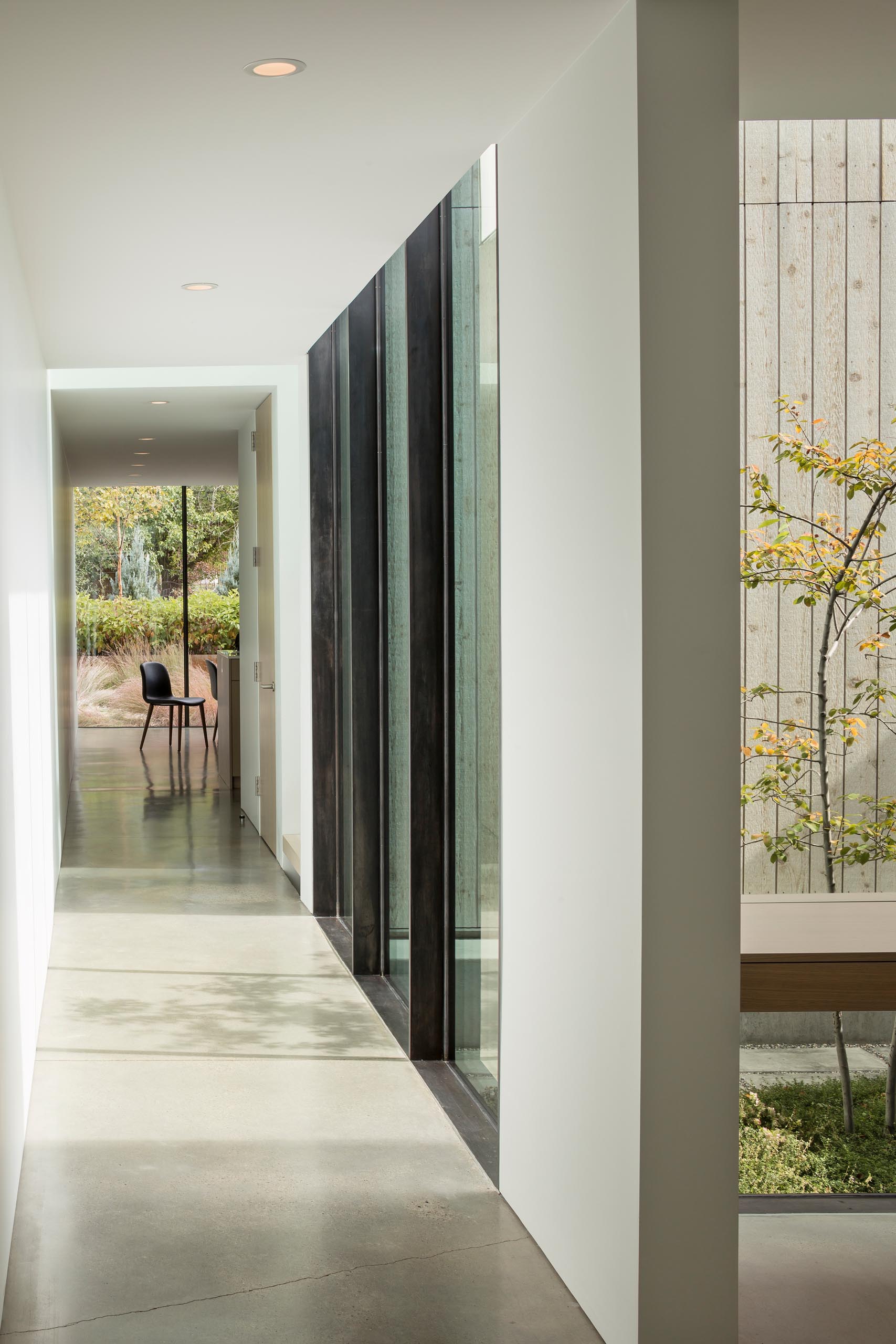 A modern home with a long hallway, floor-to-ceiling windows, and concrete floors.