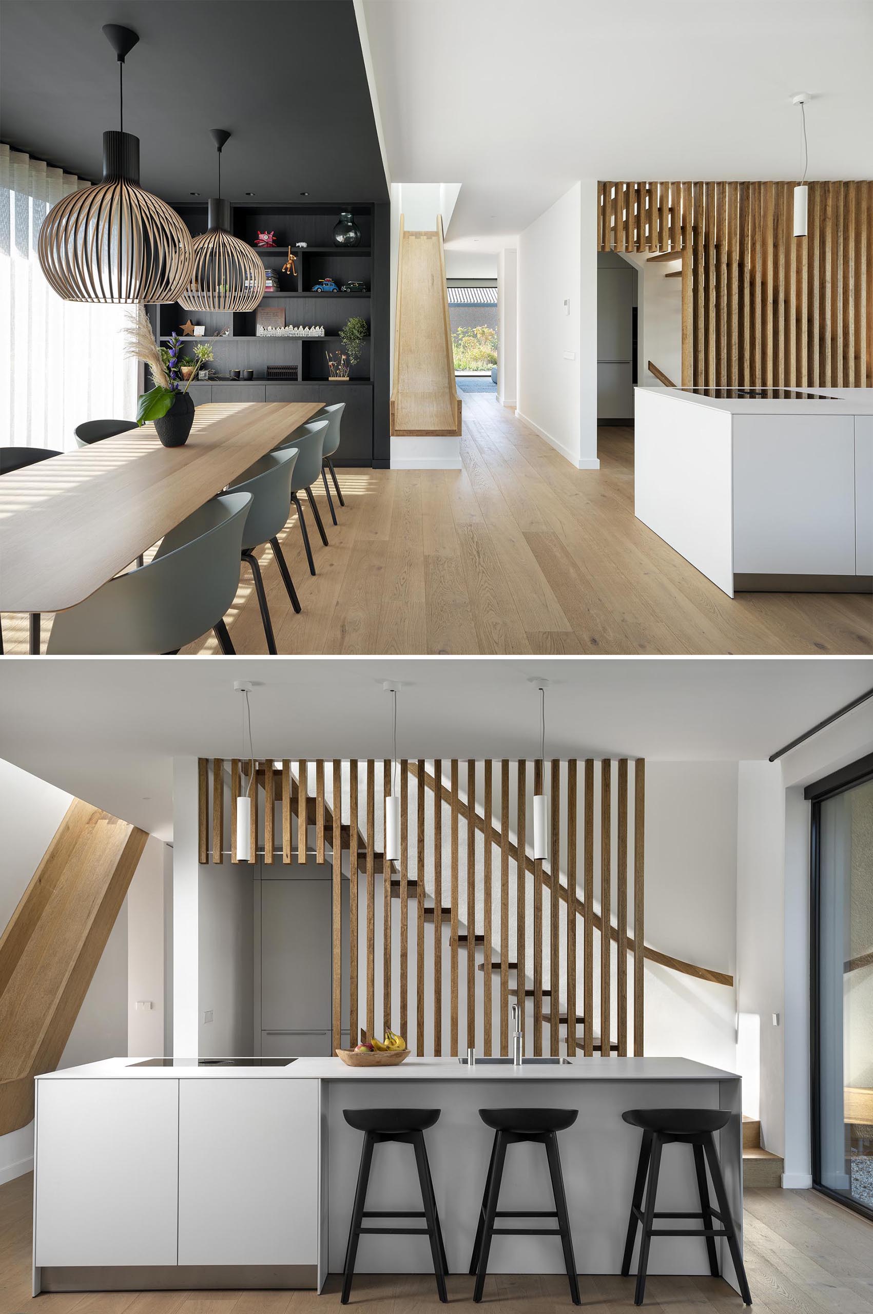 A modern home with an open plan dining room and kitchen. Black has been used on the wall and ceiling to define the dining room, while the kitchen has a wood slat backdrop that acts as a safety barrier for the stairs.