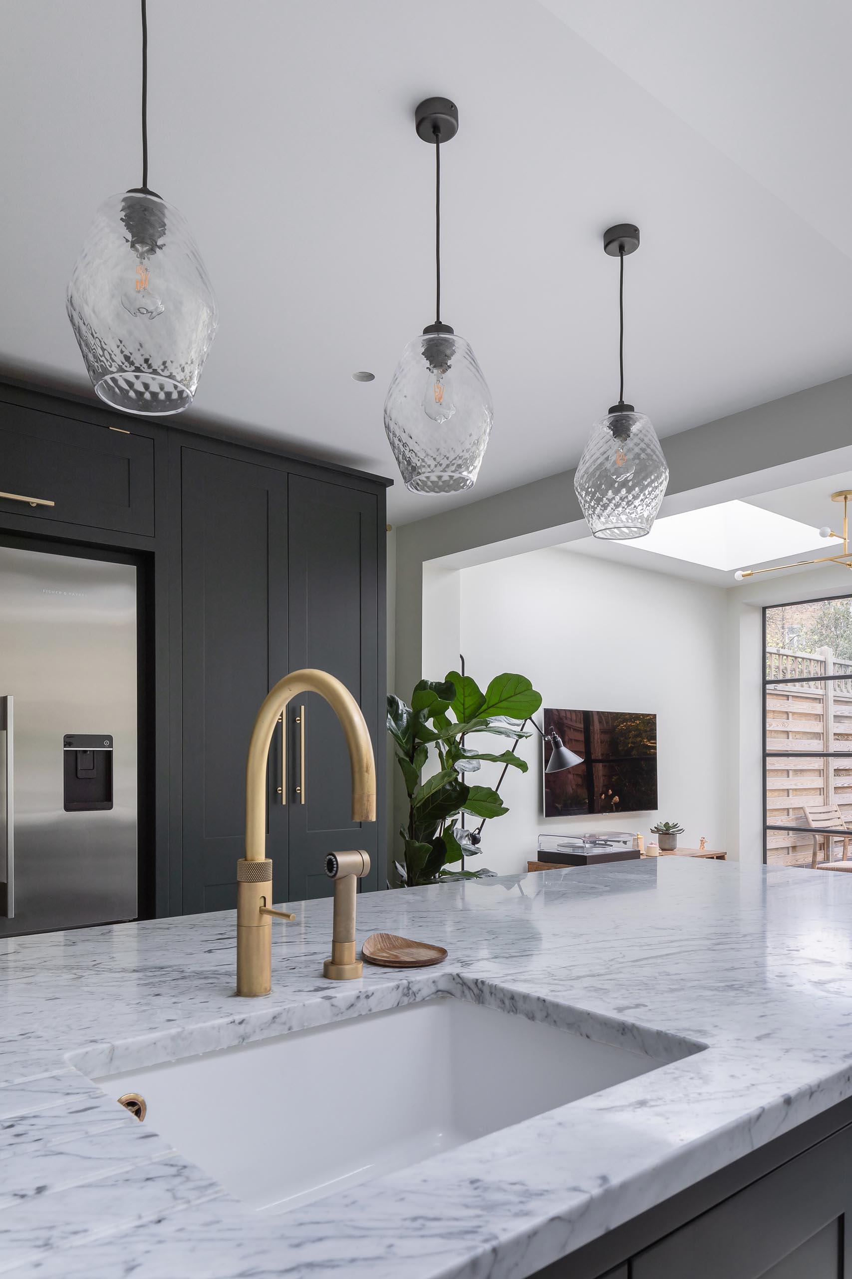 A modern kitchen with dark cabinets that have been paired with gray marble countertops and brass fixtures.