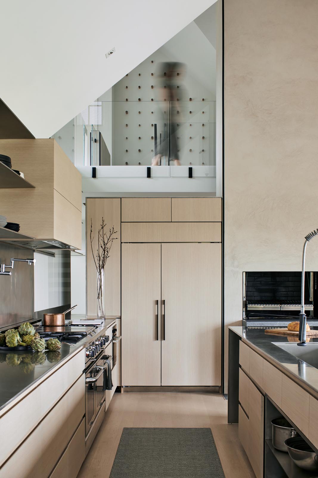 In the kitchen, there's minimalist light wood cabinets and a long island with black pendant lights and room for multiple stools.