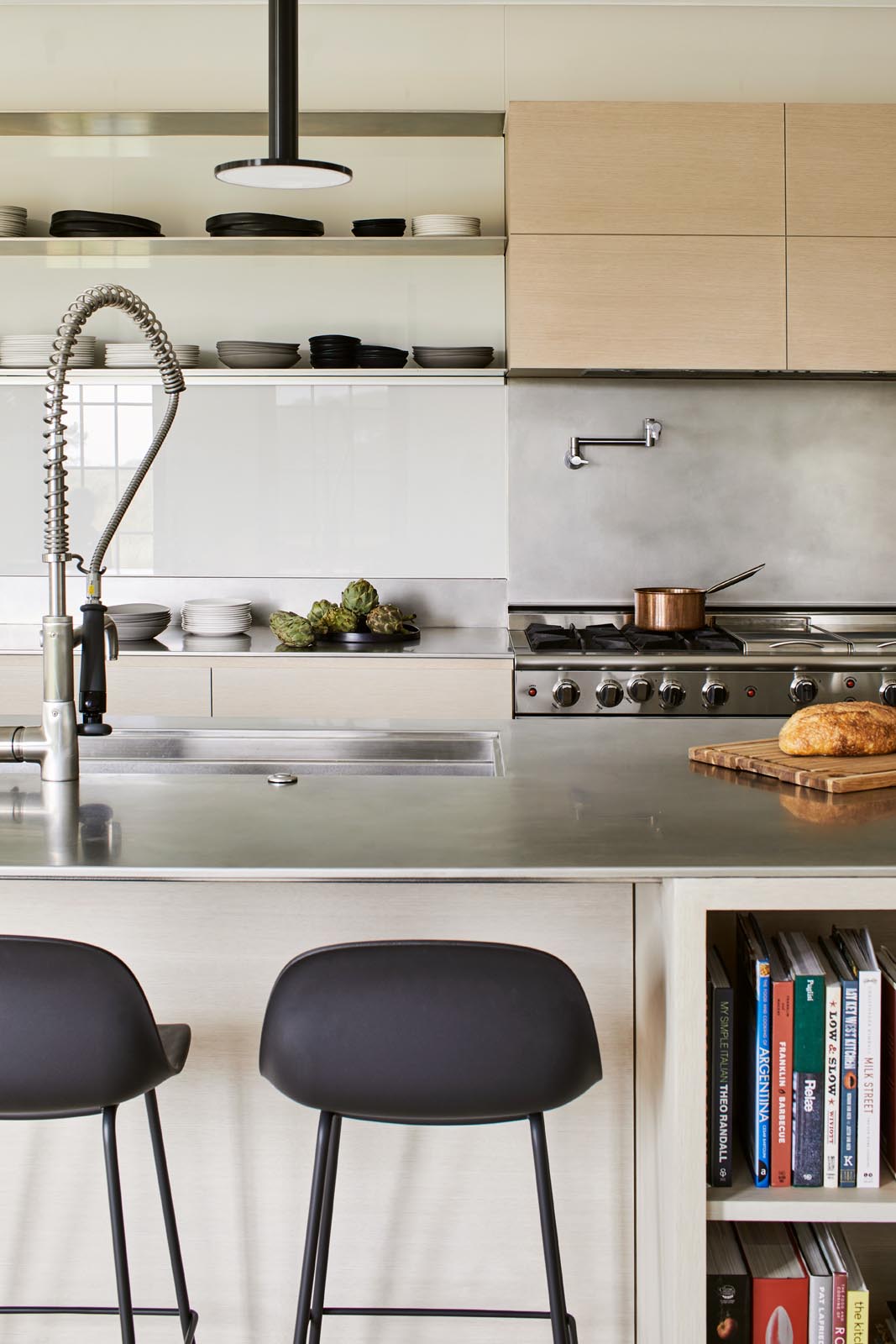 In the kitchen, there's minimalist light wood cabinets and a long island with black pendant lights and room for multiple stools.