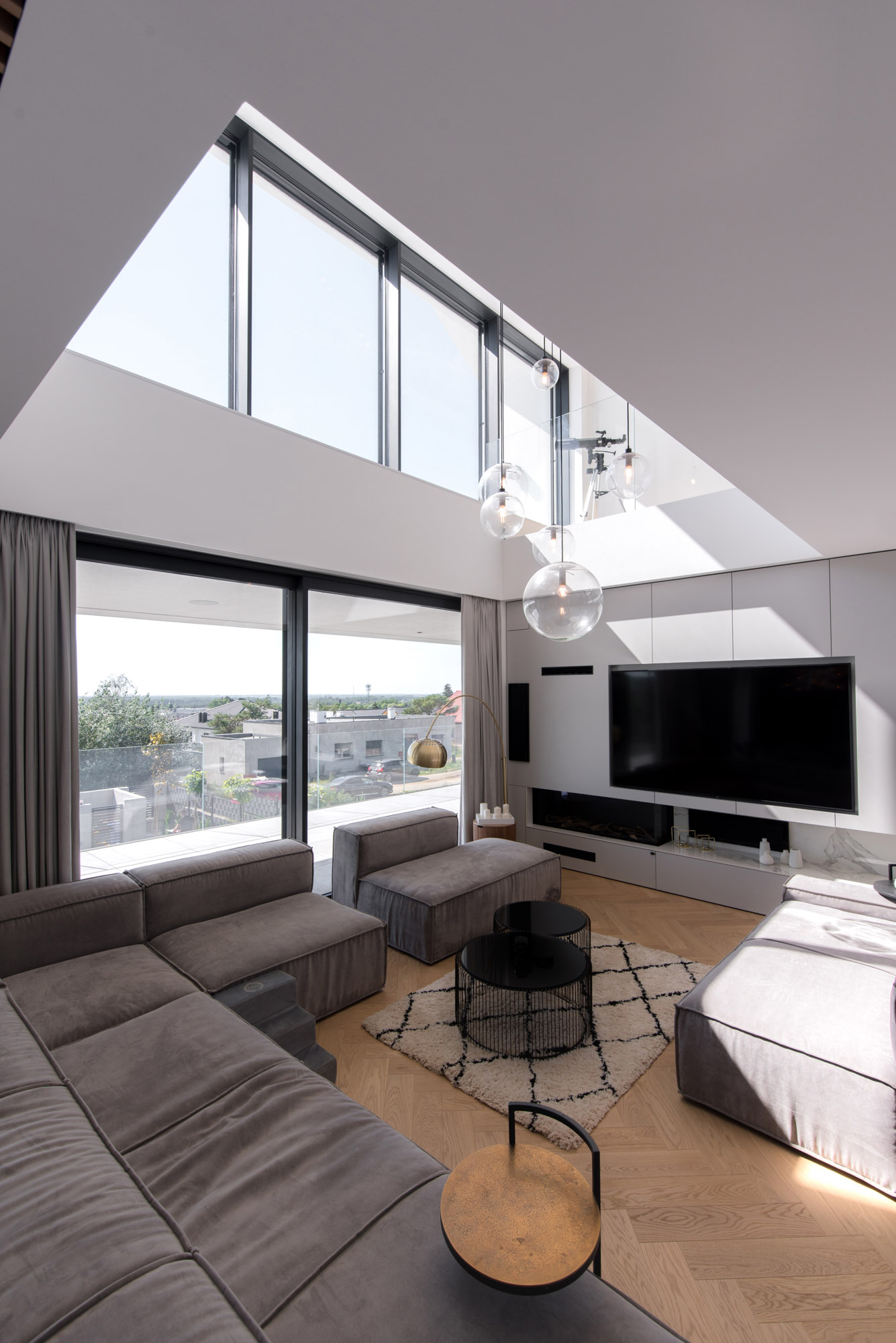A living room that's furnished with a large modular sofa, creating plenty of room for relaxing. A double height ceiling void allows the natural light from the upper windows to filter through.