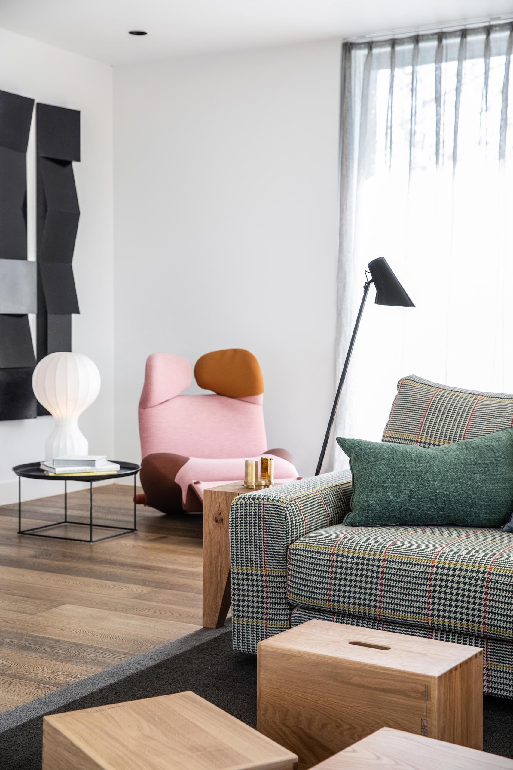 Tucked into the corner behind the living room is a small reading nook that includes a sculptural pink chaise, vertical art pieces, and a wall-mounted bookshelf.