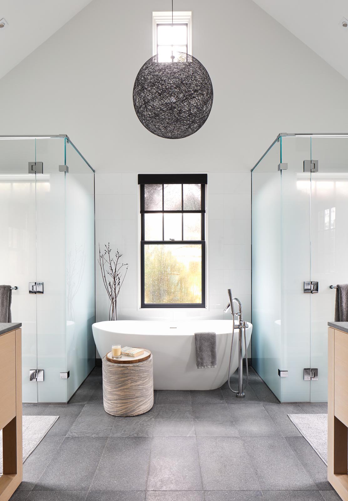 In this modern master bathroom, there's a freestanding bathtub that rests in front of the window, while frosted glass hides the showers.