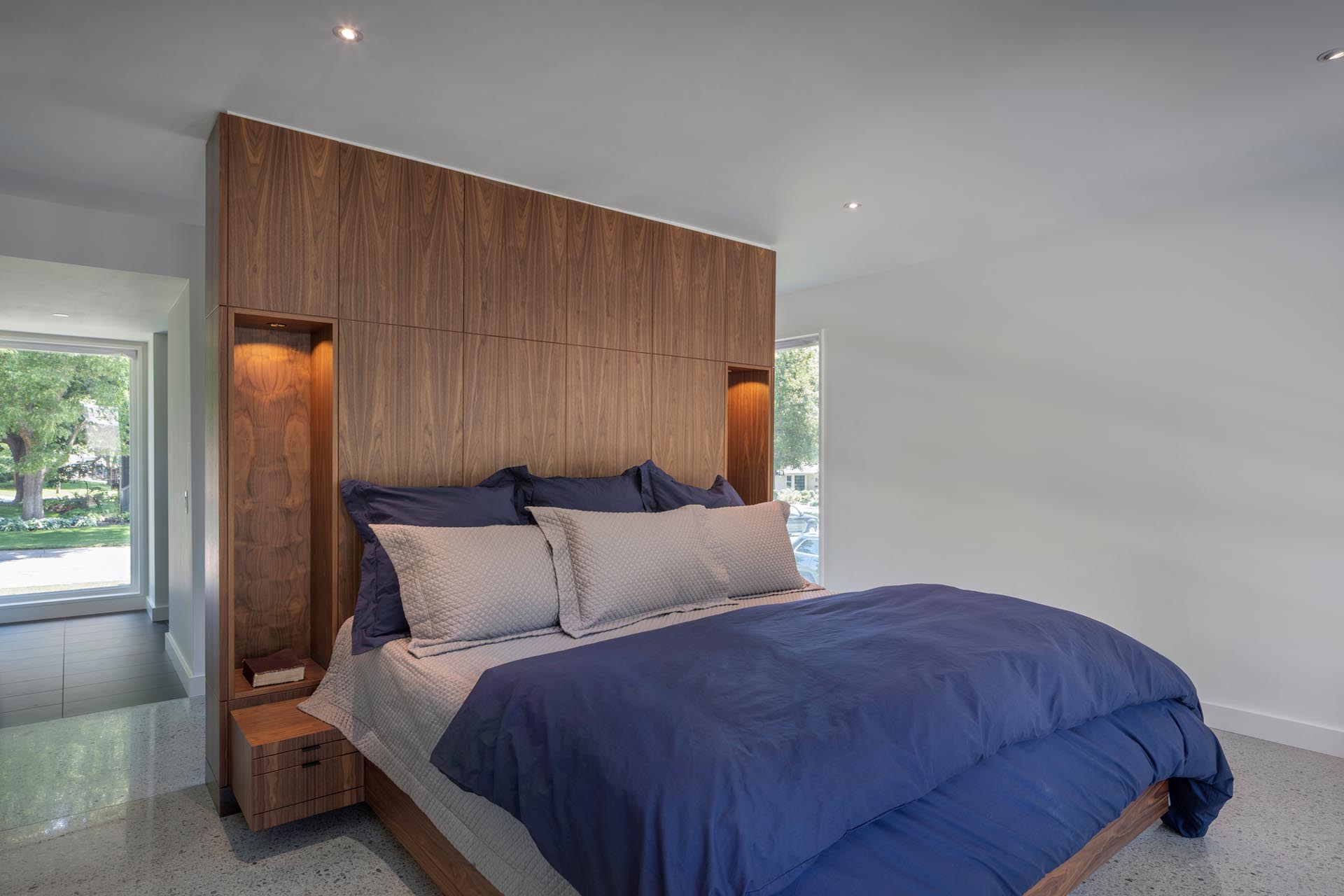 A modern bedroom with a a wood accent wall that has voids, allowing for built-in bedside lamps.