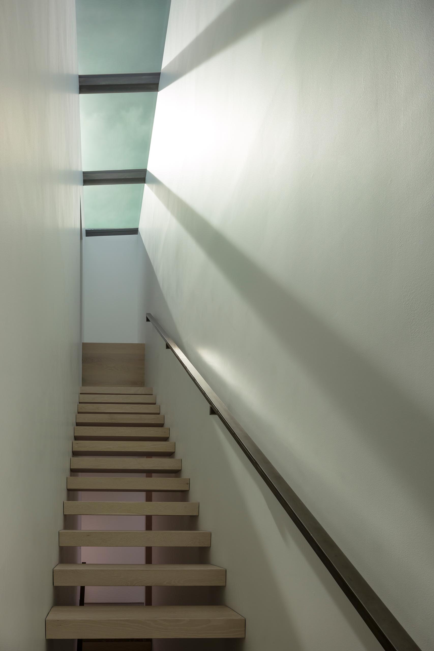 A modern staircase with metal handrail and skylights.