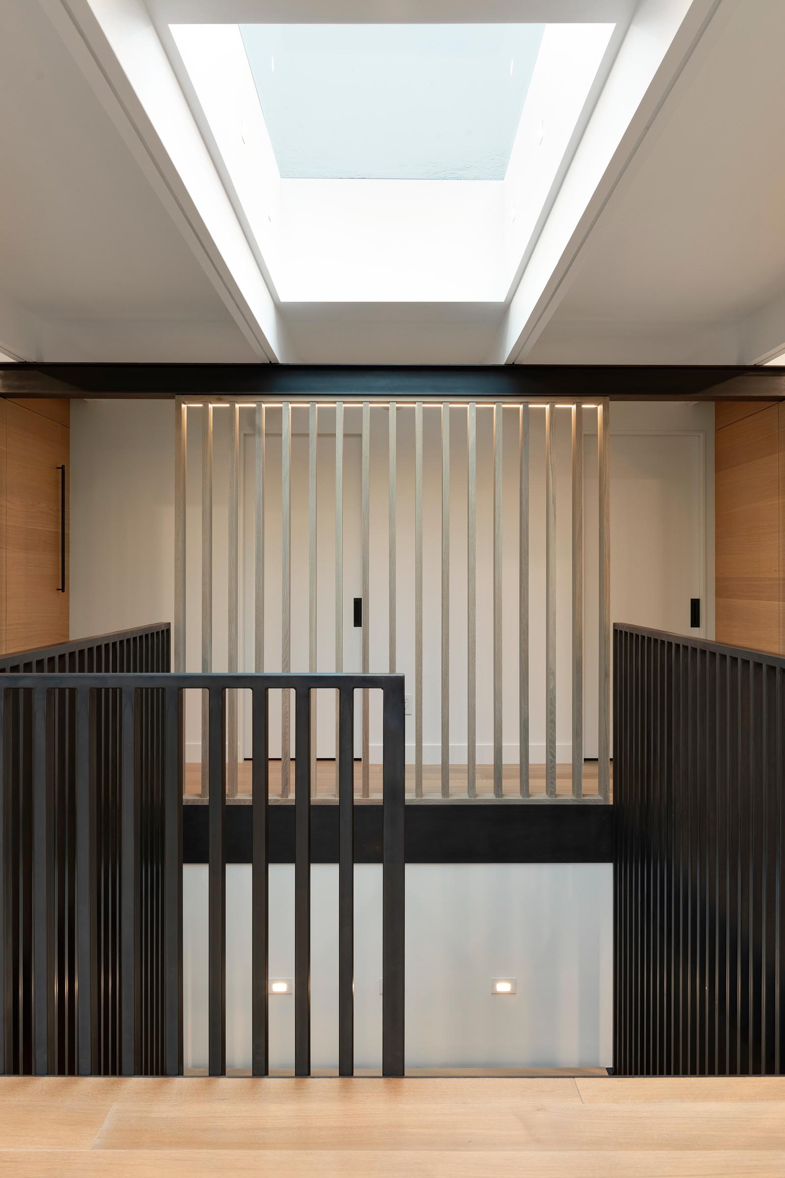A skylight by the front door filters natural light through to the staircase that leads to the lower level of the home and features black handrails.