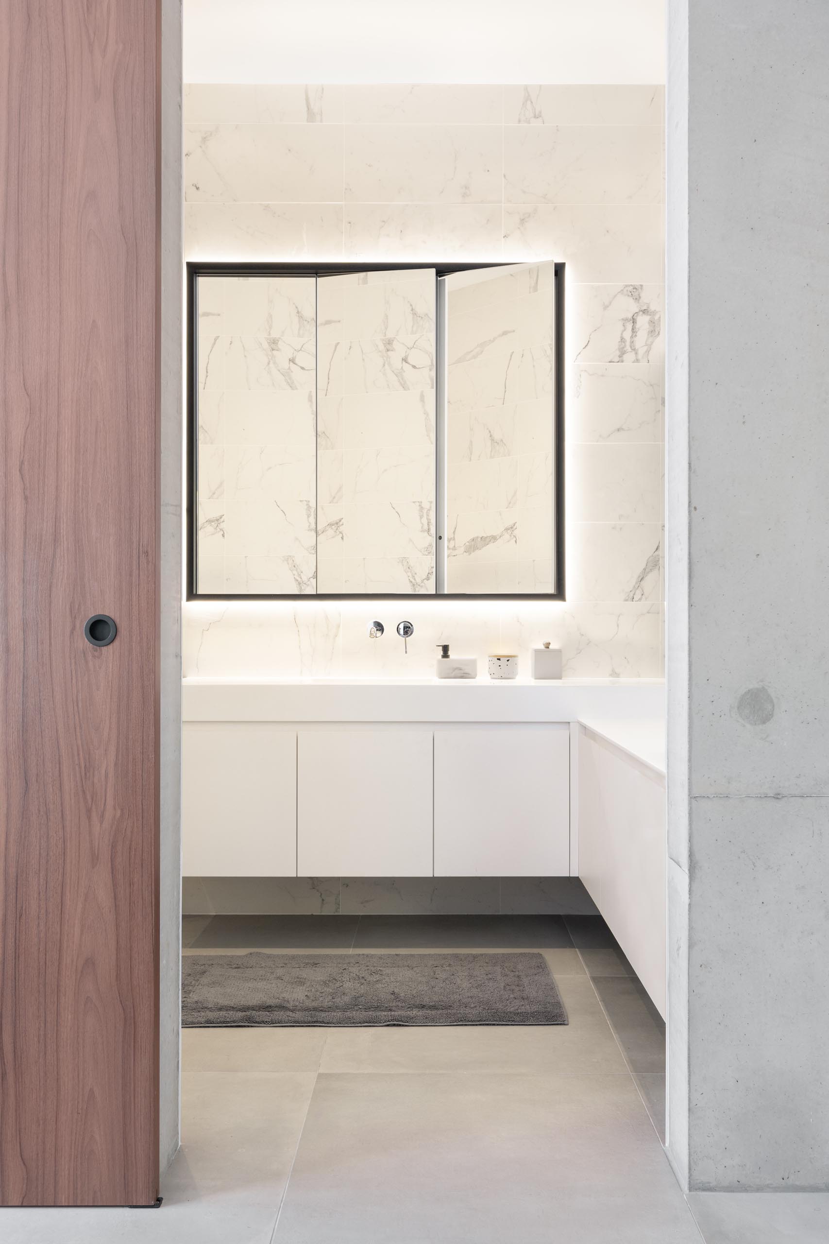 A modern bathroom with light colored walls, white cabinetry, a large mirror, and built-in bathtub.