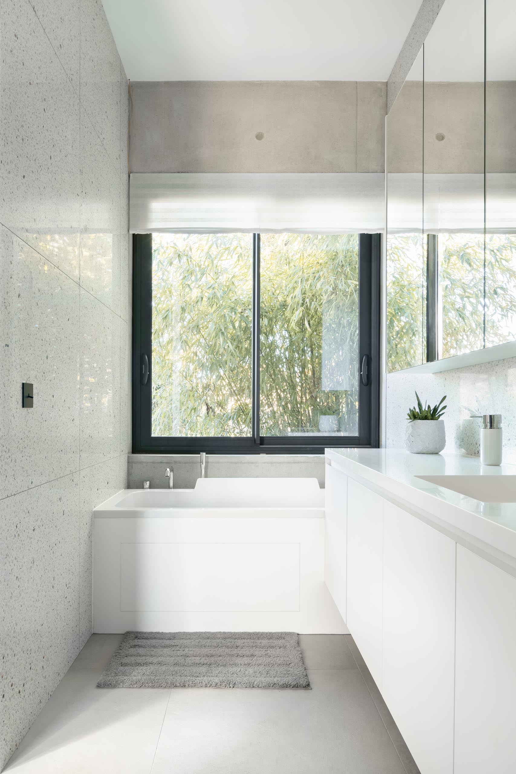 A modern bathroom with light colored walls, white cabinetry, a large mirror, and built-in bathtub.