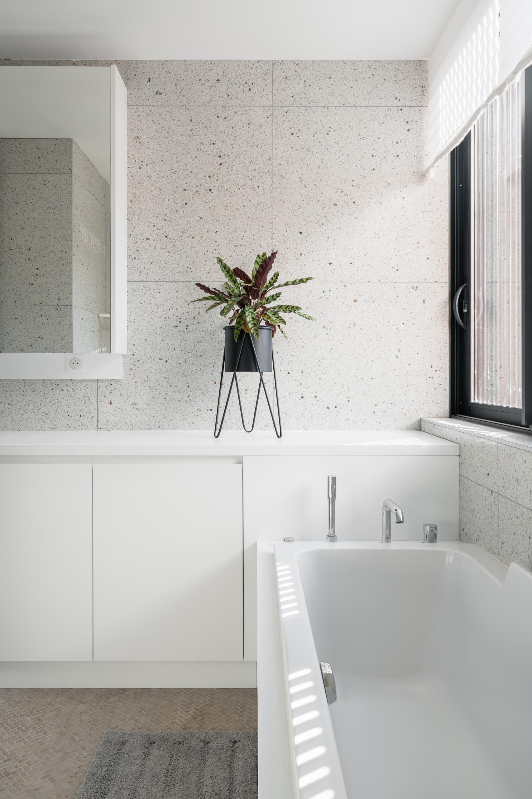 A modern bathroom with light colored walls, white cabinetry, a large mirror, and built-in bathtub.