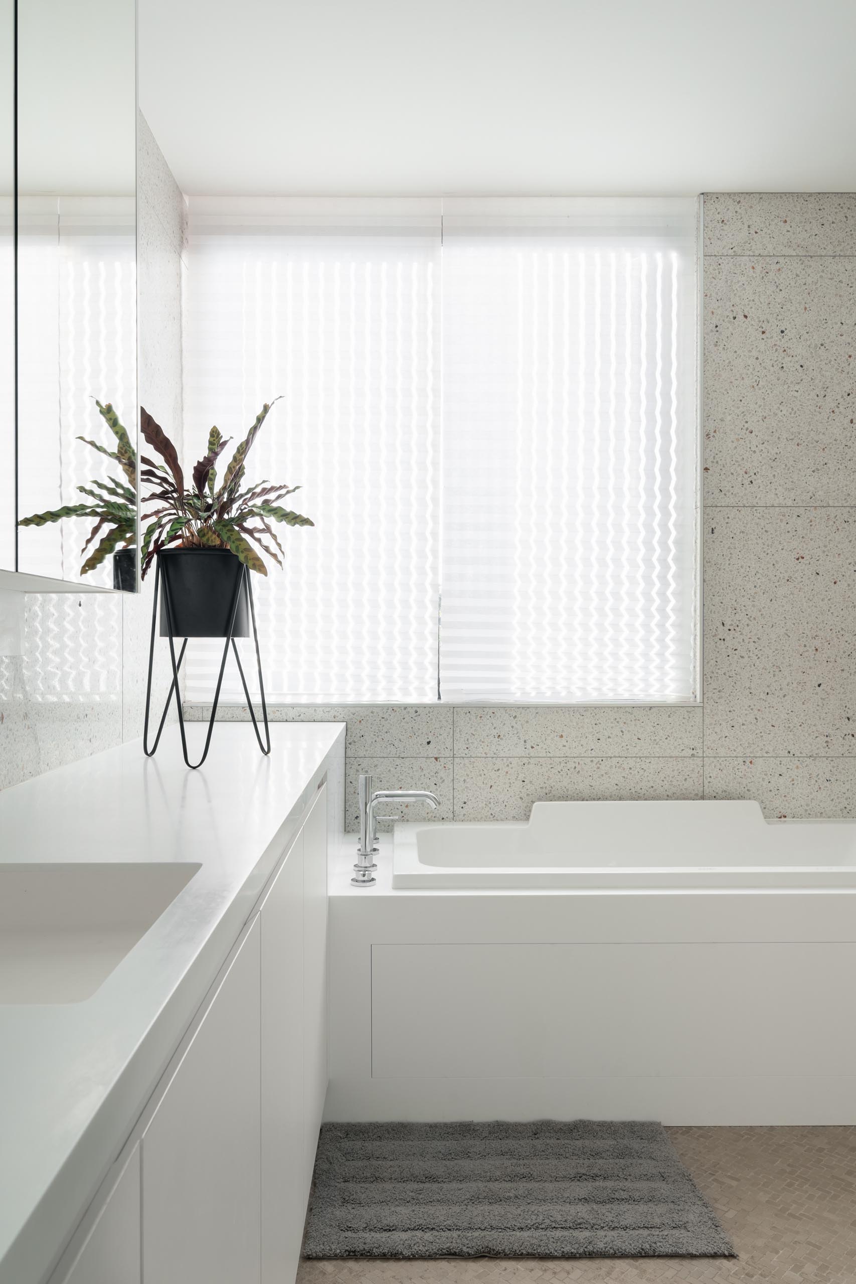 A modern bathroom with light colored walls, white cabinetry, a large mirror, and built-in bathtub.