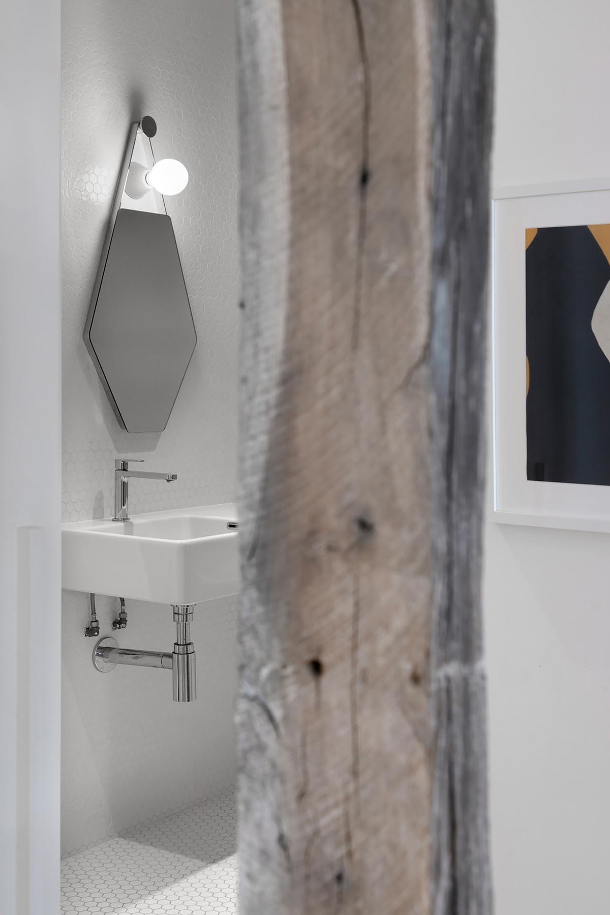 A modern white bathroom with small white hexagonal tiles and exposed original woodwork.