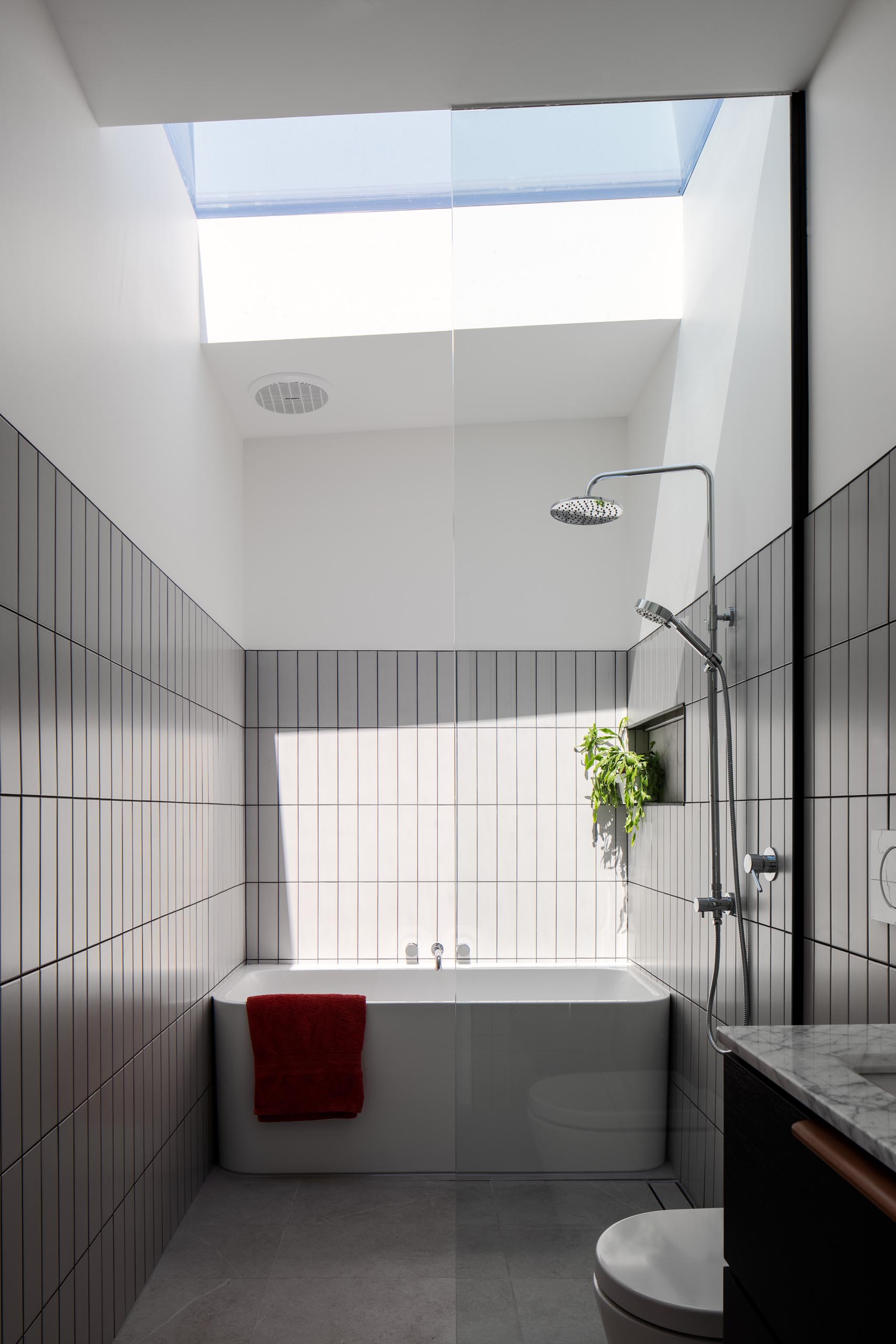 A modern bathroom with gray tiles, a white bathtub, and a skylight.