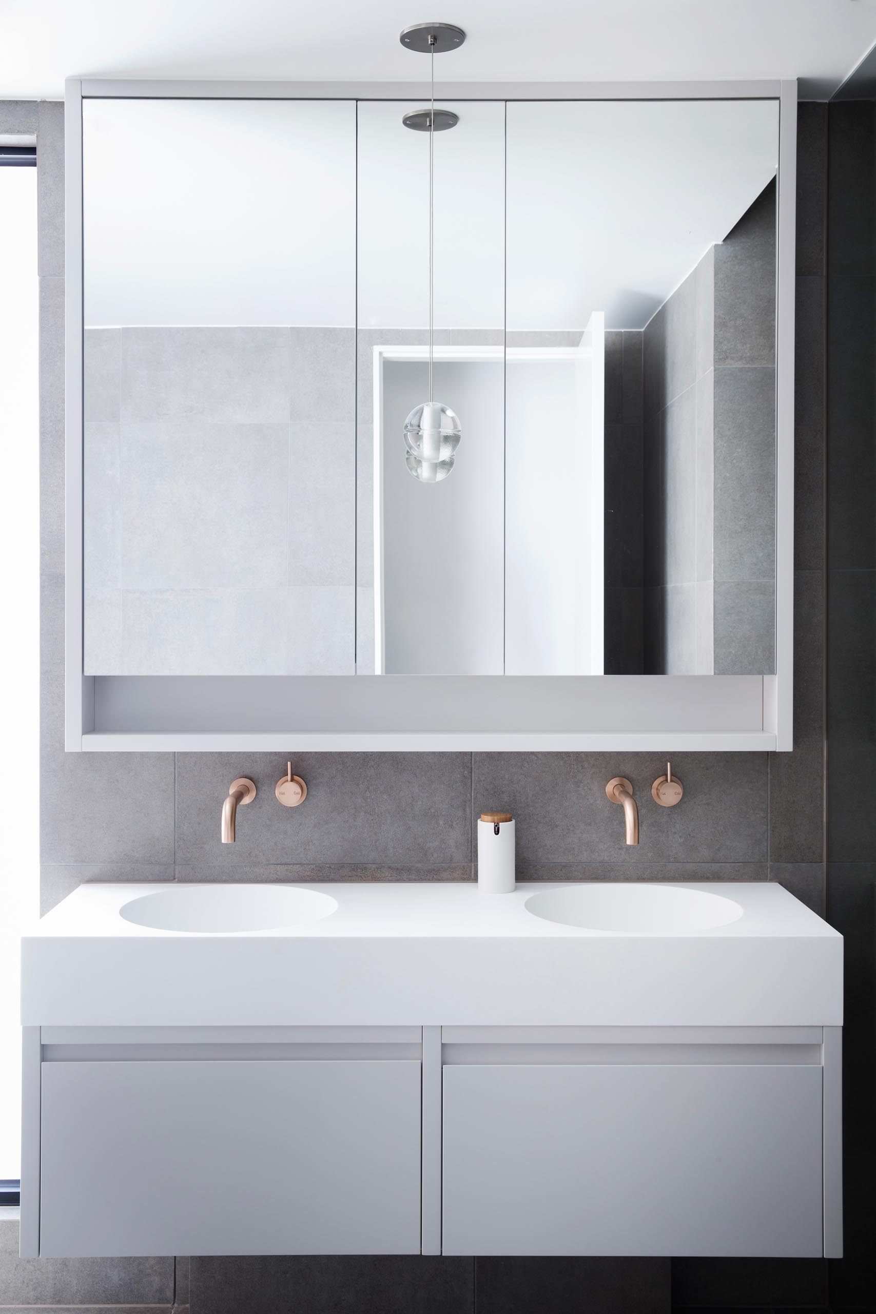 A modern bathroom with a large mirror, brushed rose gold hardware, a countertop with dual built-in sinks, and minimalist cabinetry.