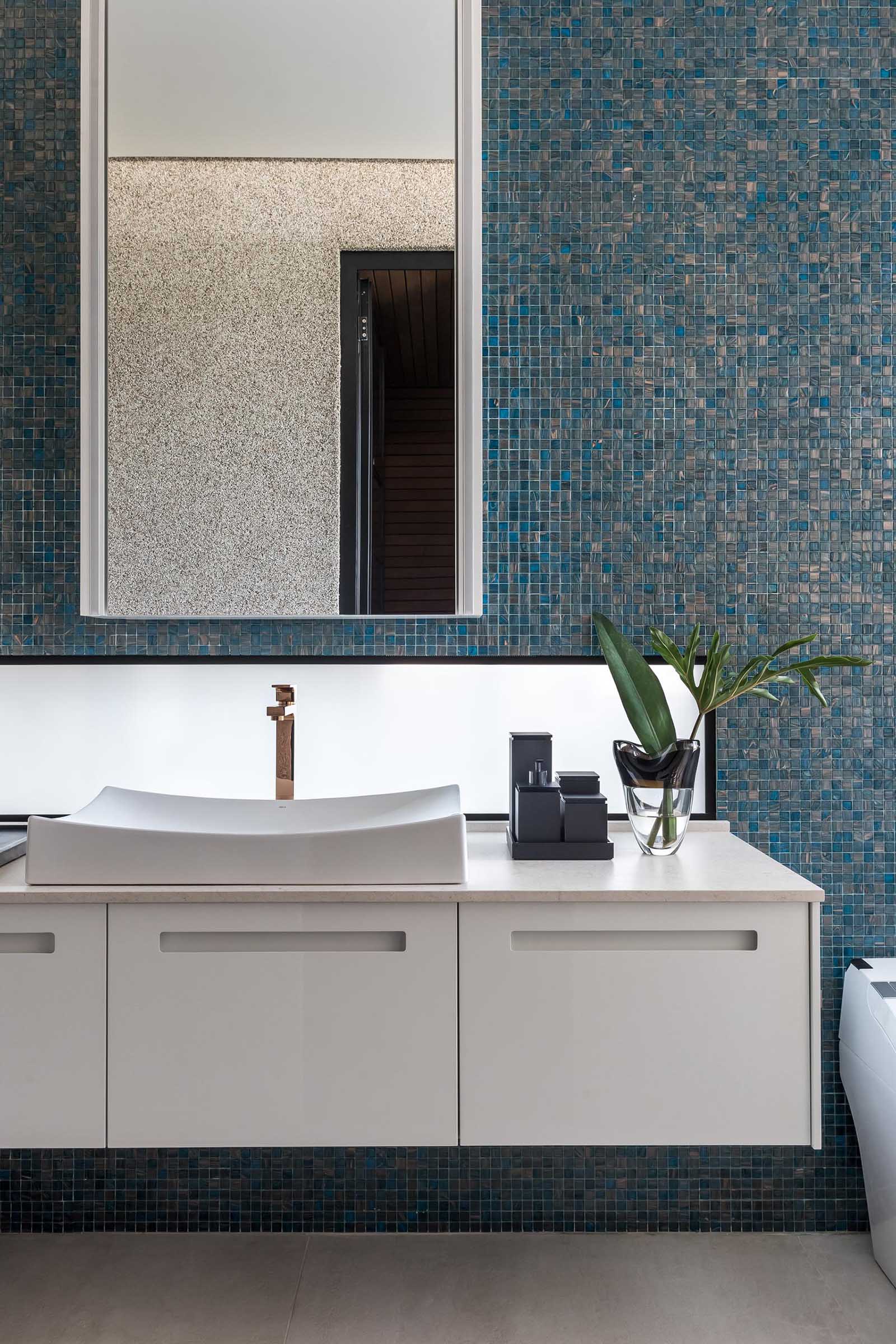 A blue tiled accent wall provides a backdrop for the white vanity and mirror in this modern bathroom.