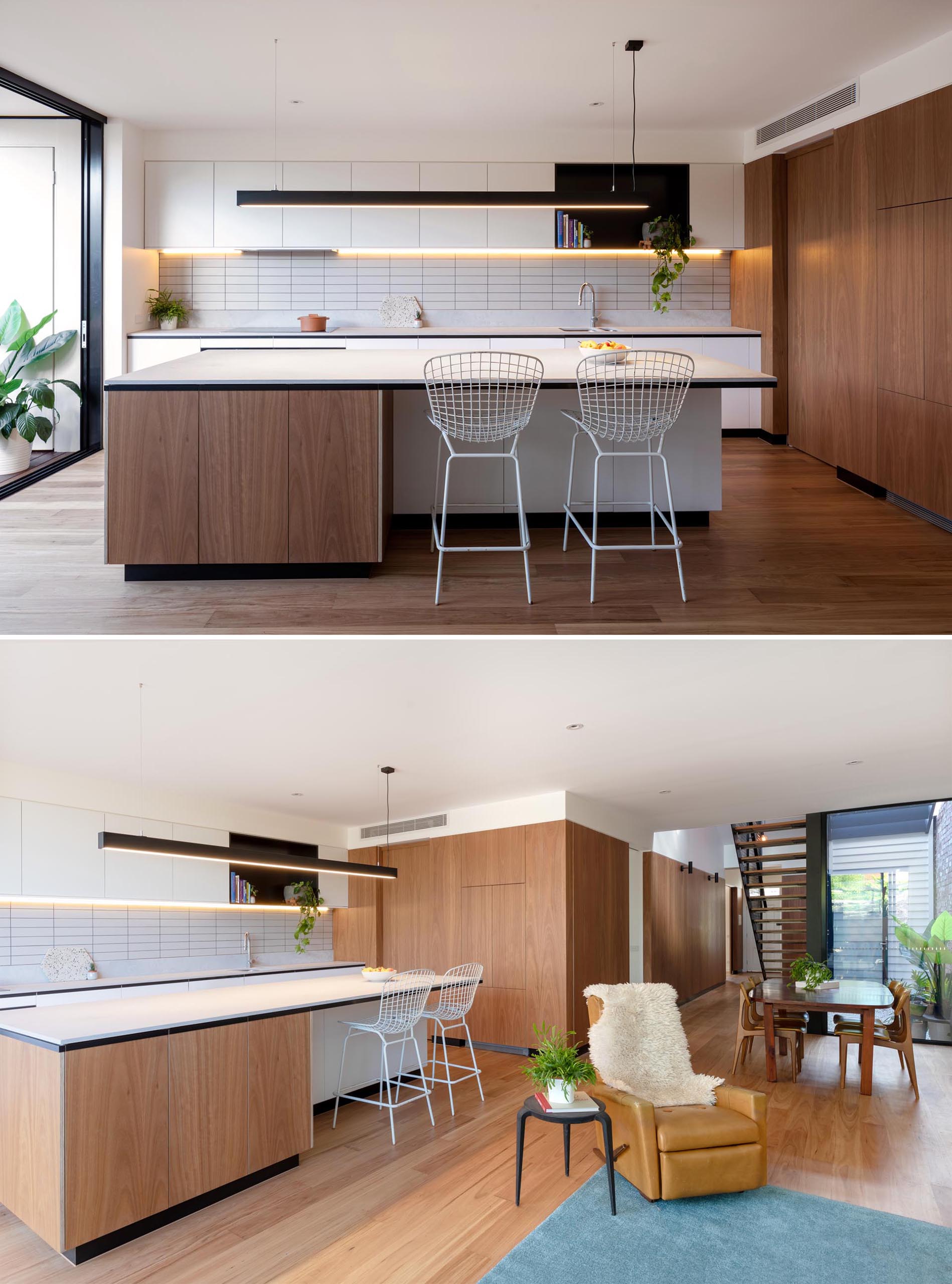 A modern kitchen includes minimalist white cabinets, a black accent shelf, a large island with room for seating, and undermount lighting.