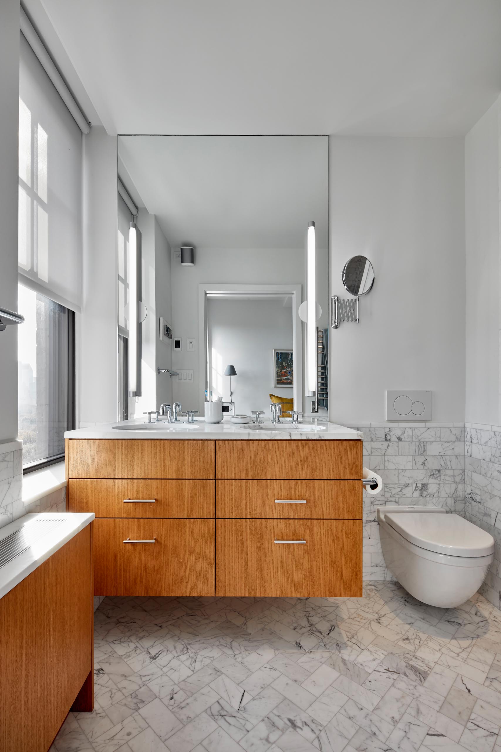 A modern bathroom with a wood vanity and radiator cover, and marbled tiles.