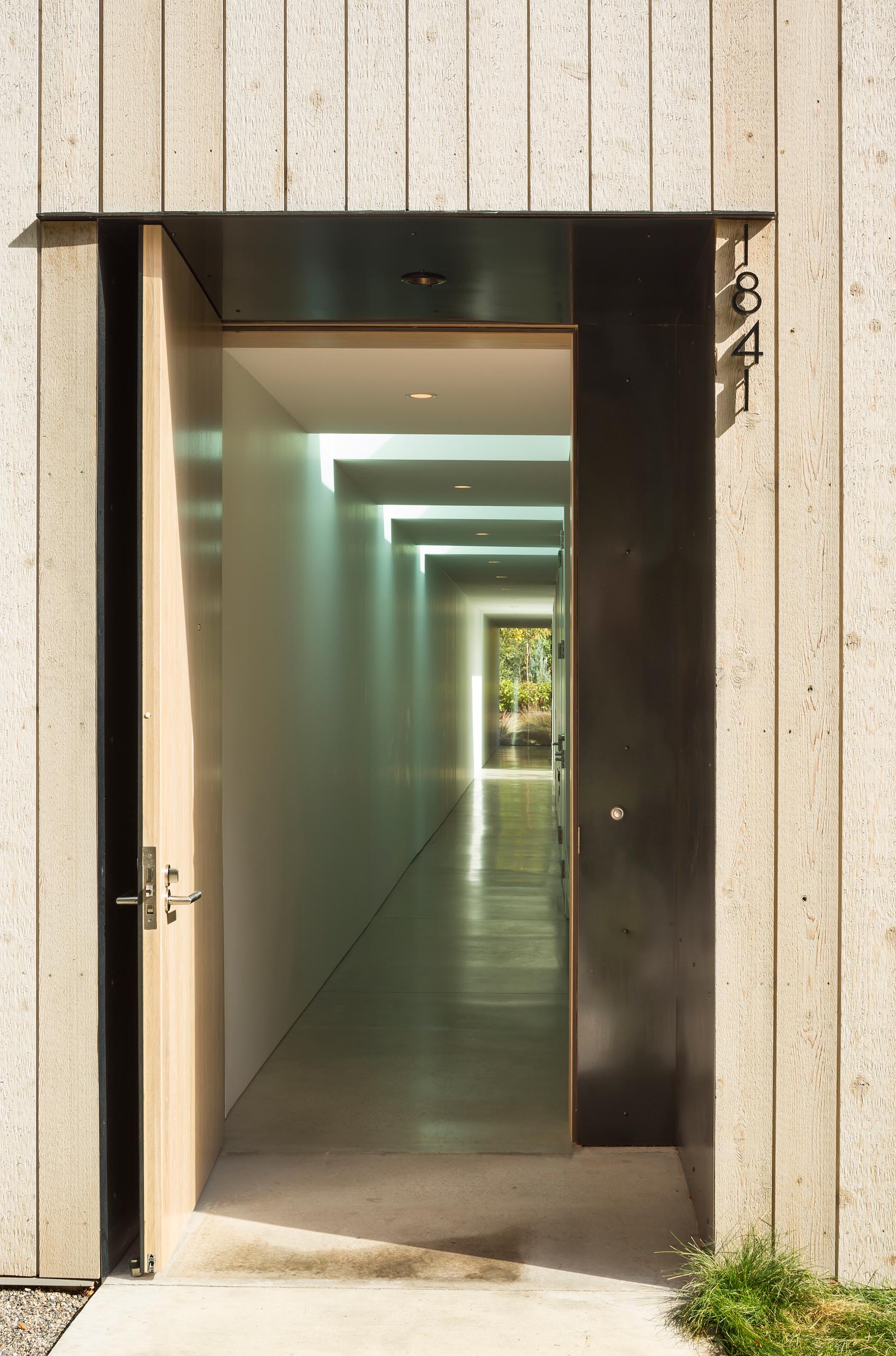 A modern cedar clad home with a black front door and long hallway.