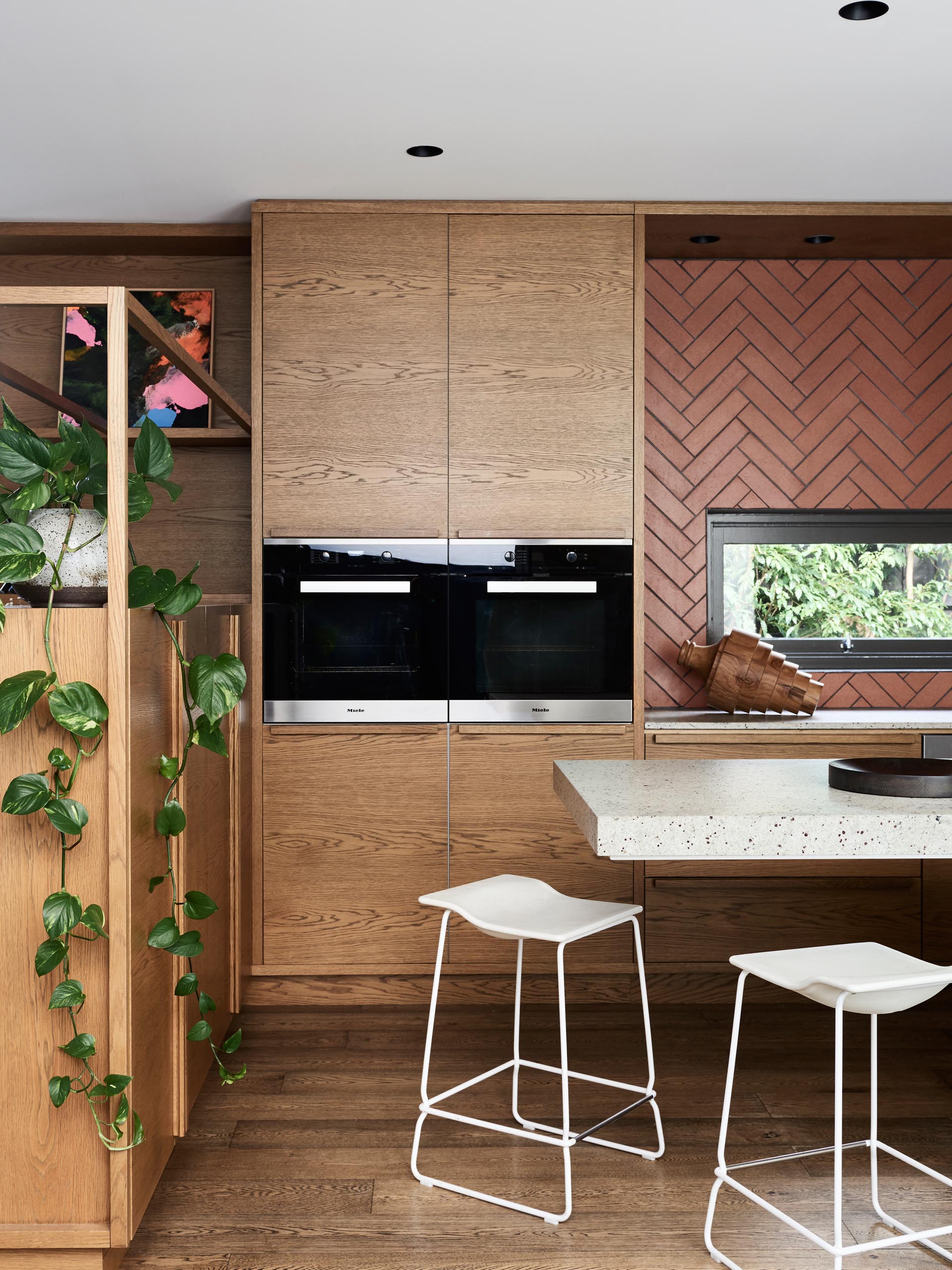 This kitchen has minimalist wood and white cabinets have been paired with a long island, and a terracotta colored tile backsplash that surrounds the window.