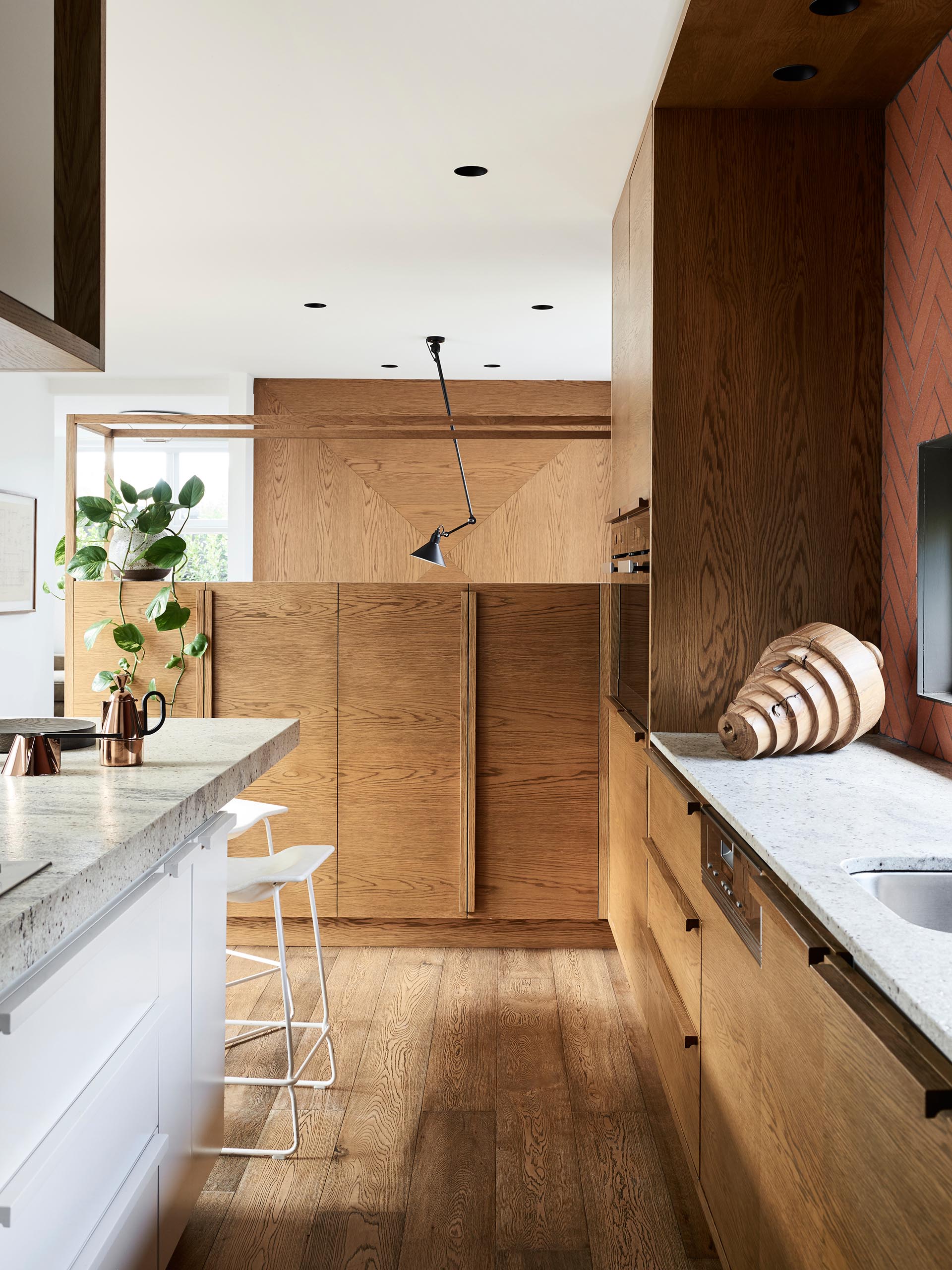 This kitchen has minimalist wood and white cabinets have been paired with a long island, and a terracotta colored tile backsplash that surrounds the window.