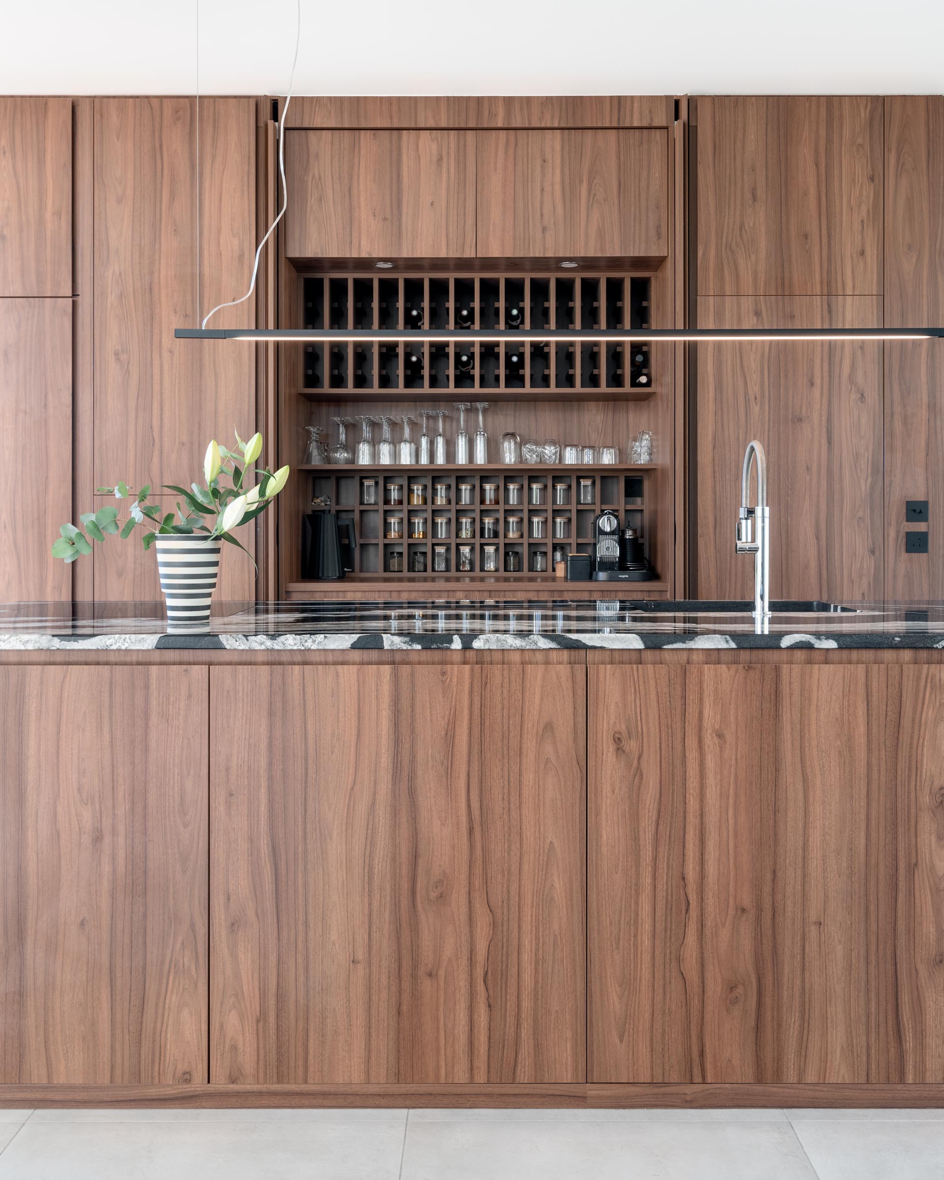 In this modern kitchen, minimalist warm wood cabinets have been used along the wall and the island. Hidden within a pair of the hardware free cabinets are shelving that's designed to hold wine bottles, glassware, and spice jars.