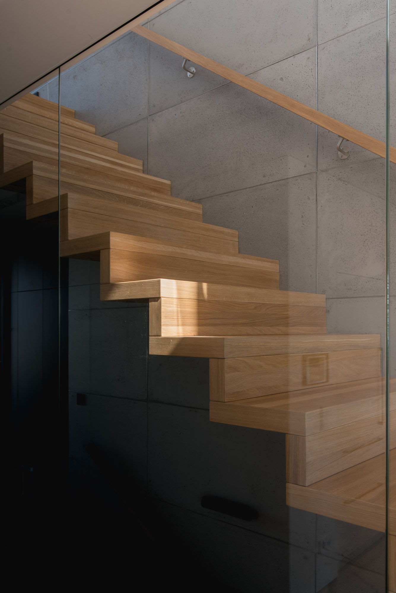 Wood stairs behind a glass wall lead from the social areas of this modern house to the upper floor.