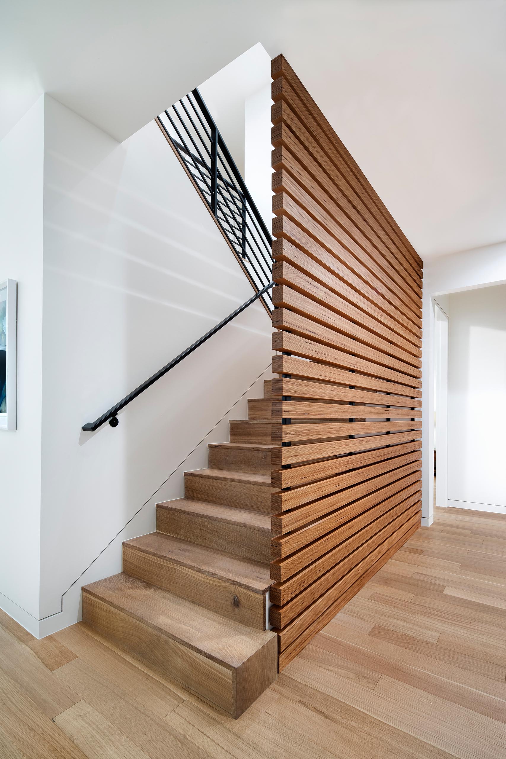 Modern wood stairs with a matching screen and black handrail.