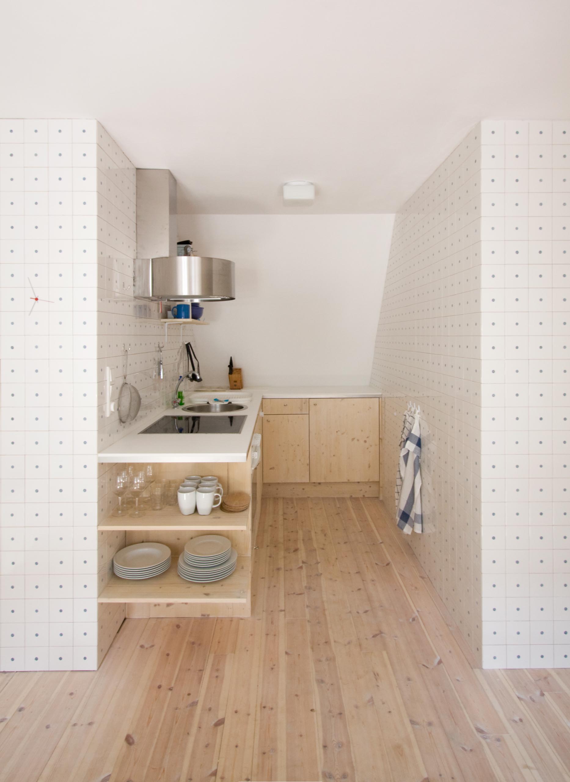 A simple and small kitchen with pine floors and cabinets, and a white countertop.