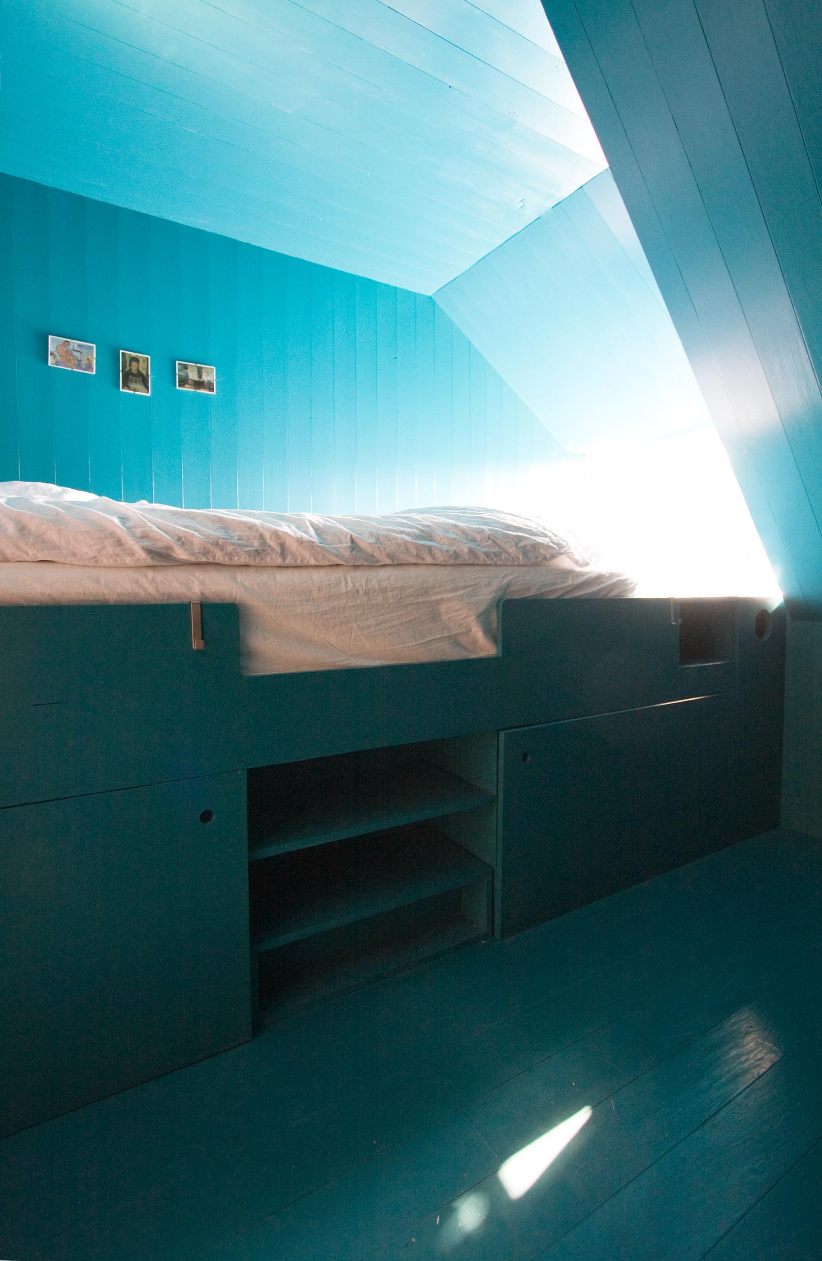 A modern turquoise blue bedroom with a loft bed that includes storage underneath.