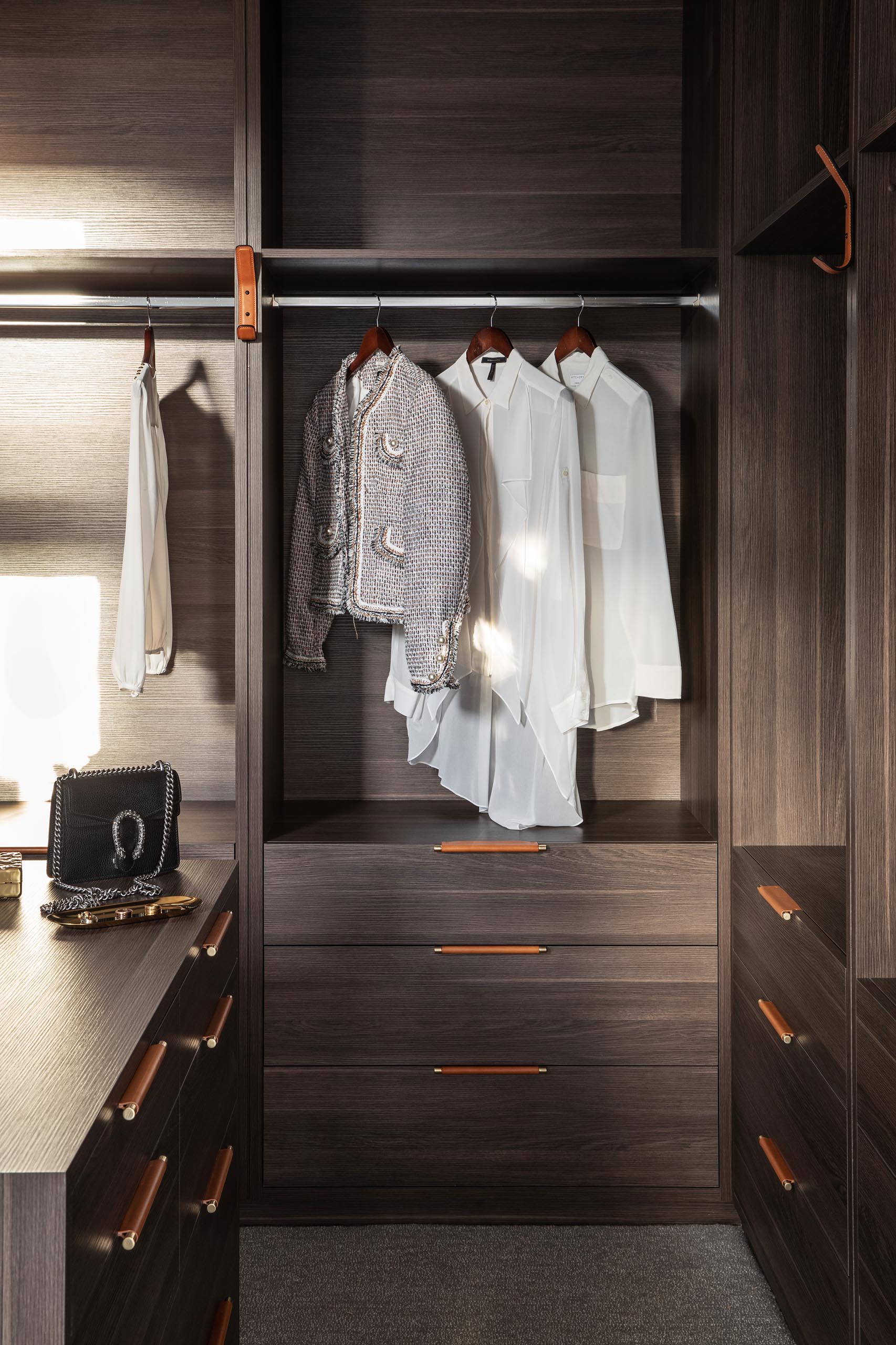 A modern walk-in closet showcases dark wood cabinetry with metal and leather drawer pulls.