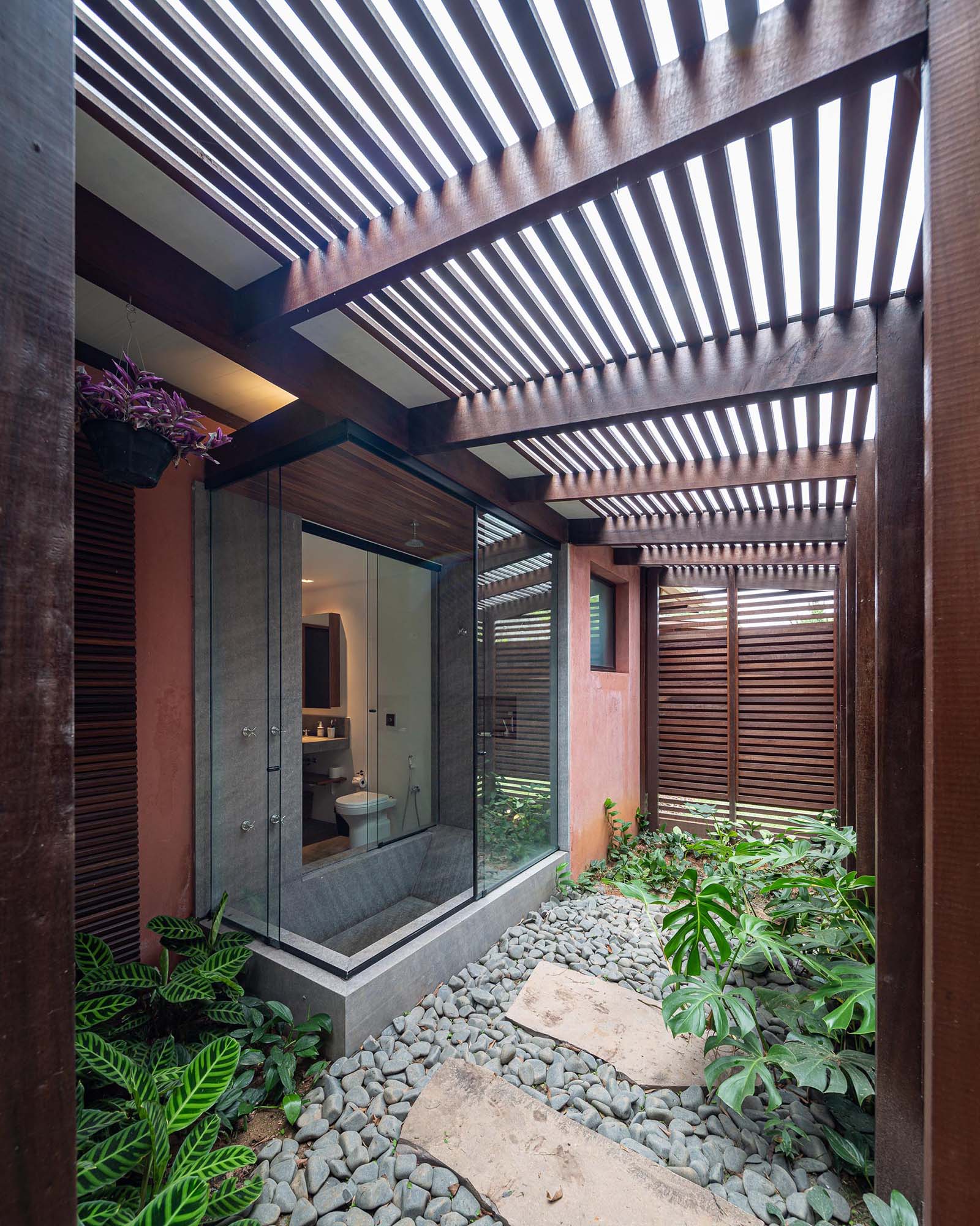 In this modern bathroom, there's a built-in sunken bathtub with sliding windows that open to a small outdoor space and garden, which is kept private by the wood slat screens.