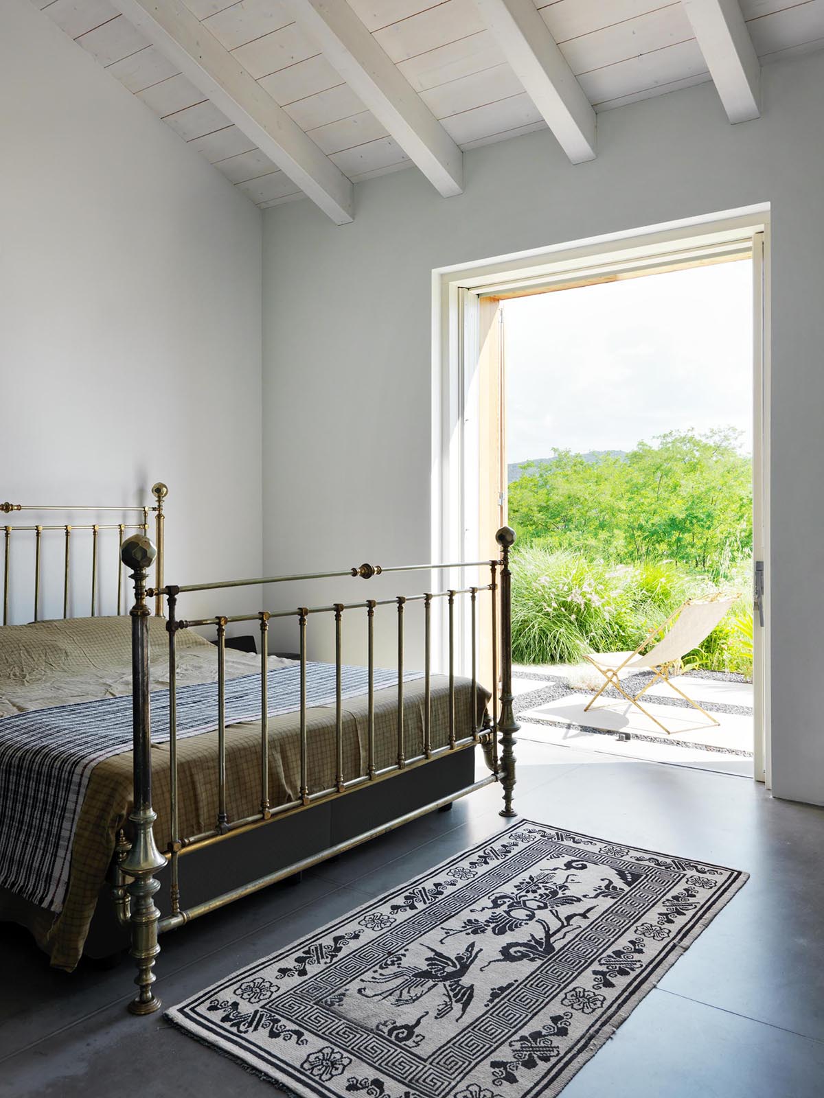 A bedroom in a modern farmhouse that has sliding doors open to a small patio.