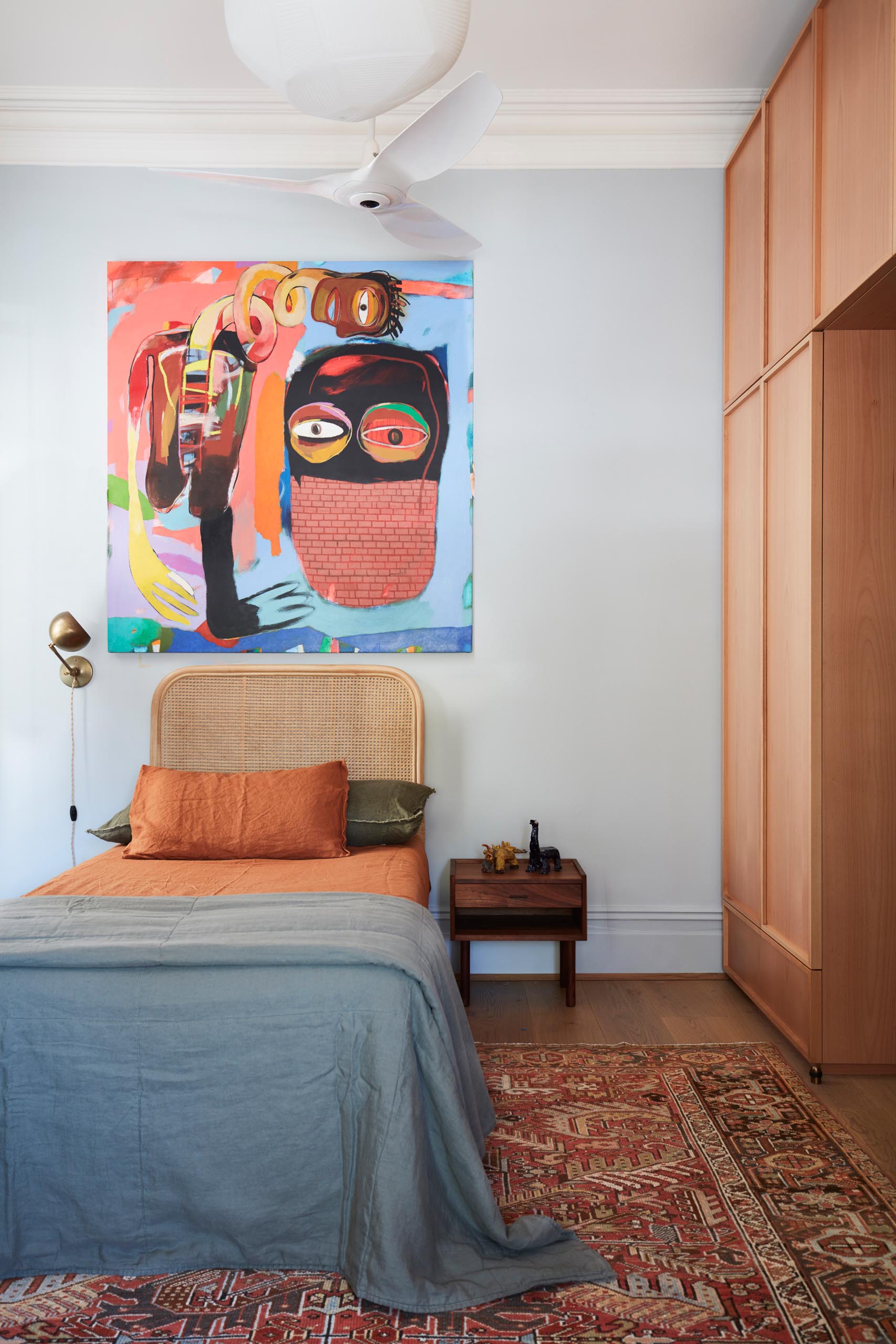 A bedroom with a bold and colorful art piece above the bed.