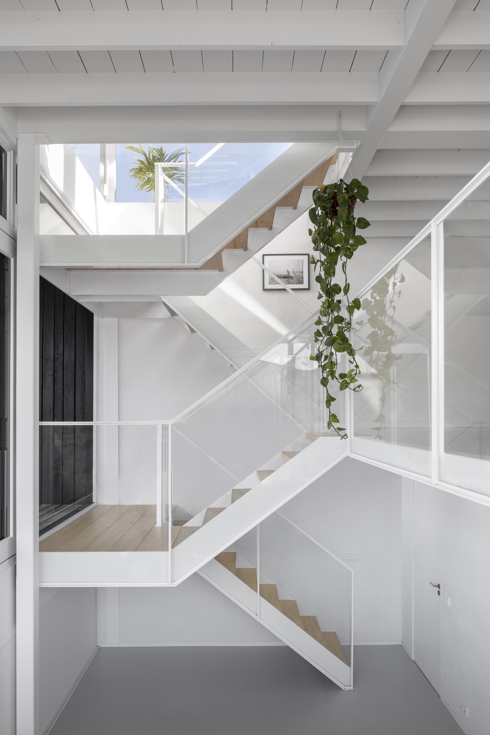 A white staircase in this modern float home matches the walls and ceiling, connects the various levels of the float home, and adds a warm wood element to the space.