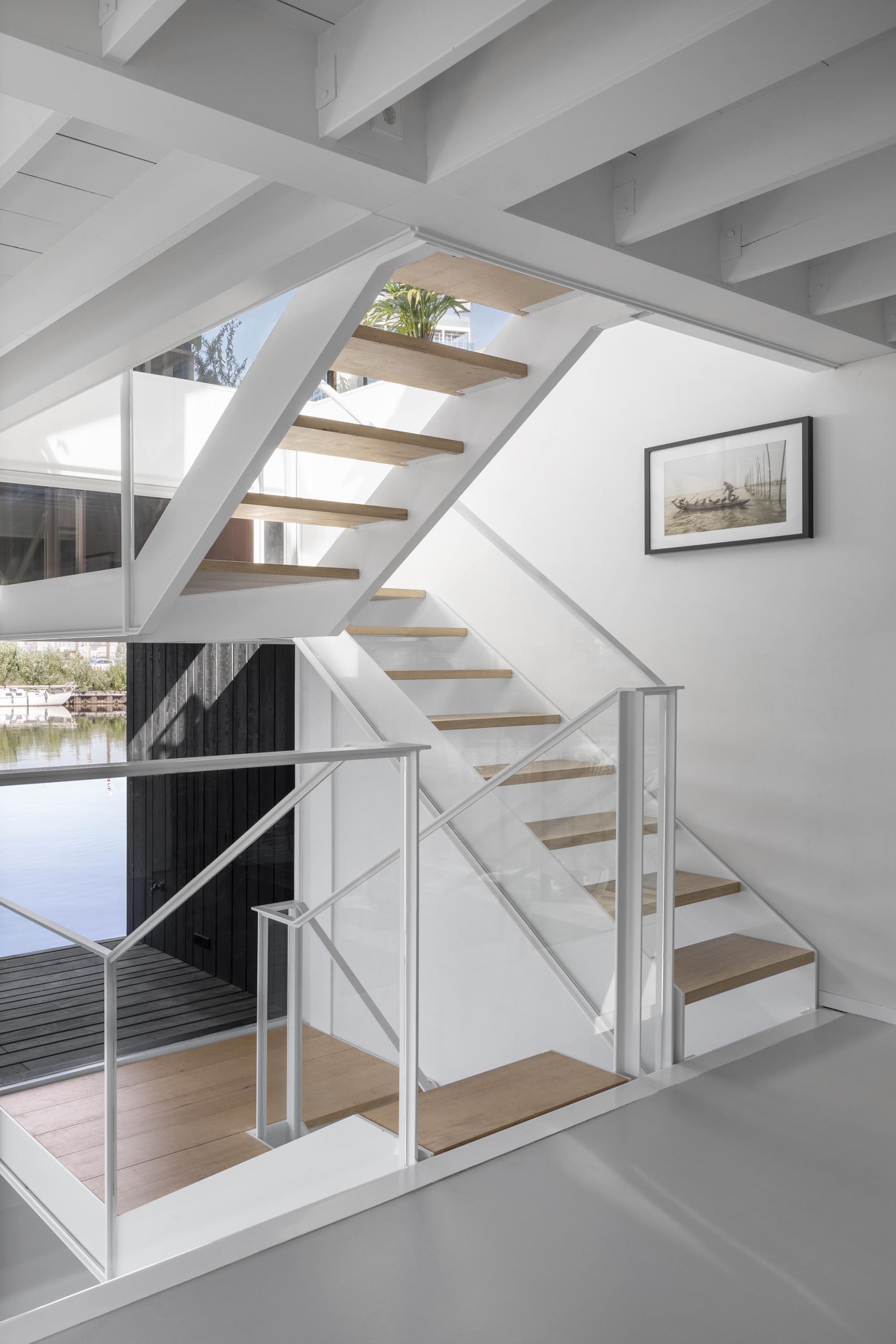 A white staircase in this modern float home matches the walls and ceiling, connects the various levels of the float home, and adds a warm wood element to the space.