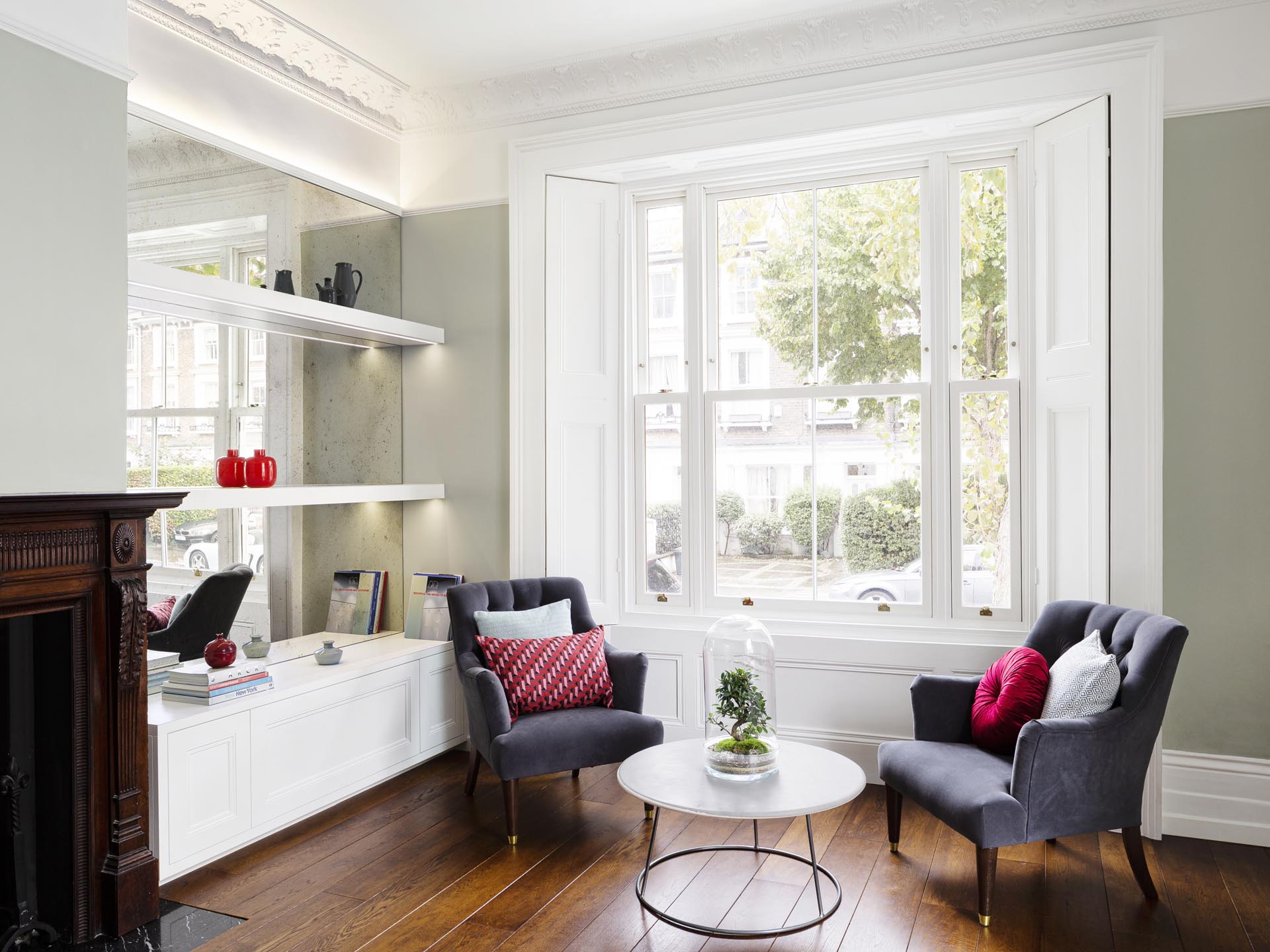 A sitting room with a mirrored wall that reflects the natural light from the window.