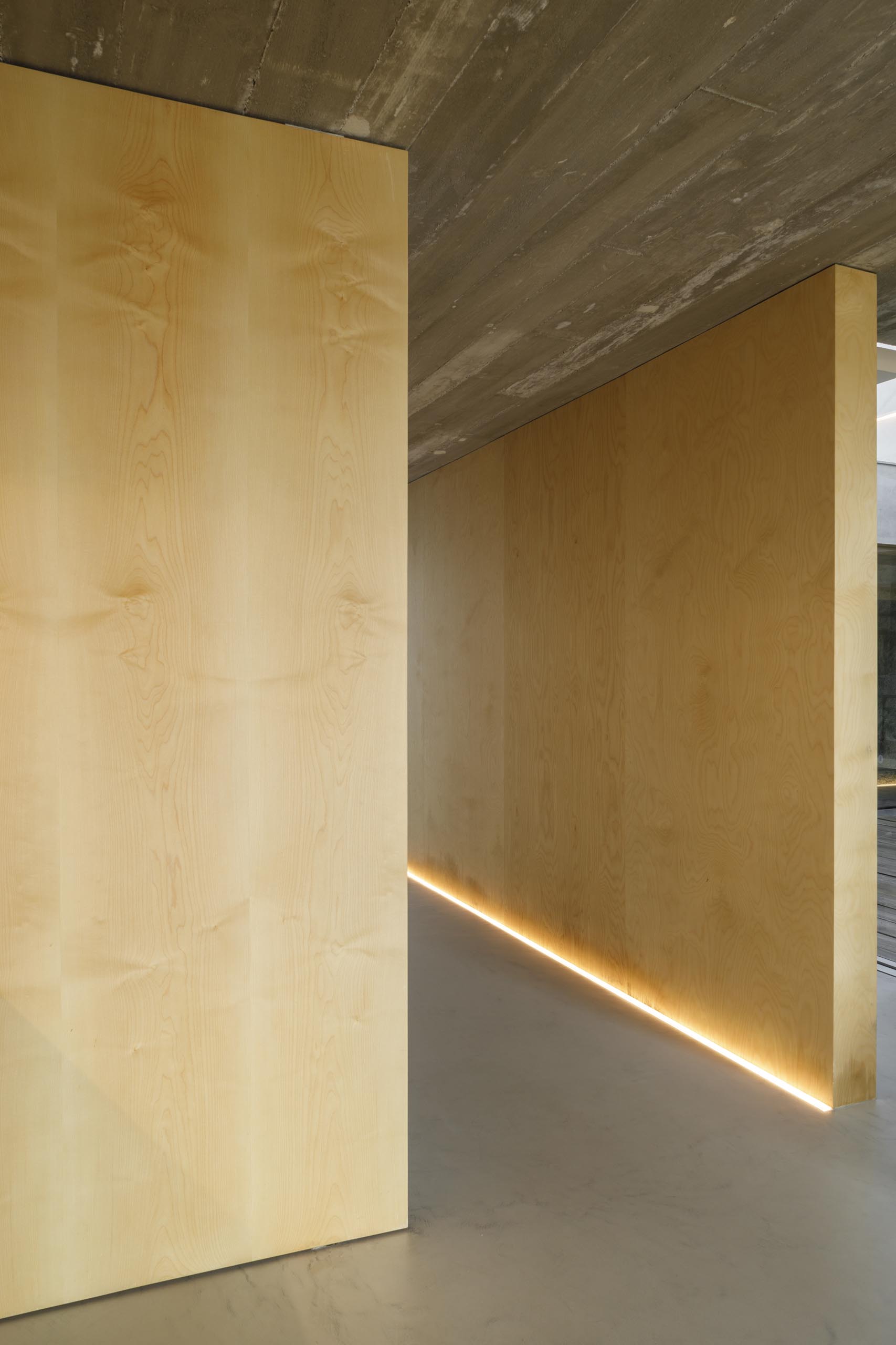 Một hành lang với những bức tường gỗ được chiếu sáng bằng hệ thống đèn LED trên sàn.