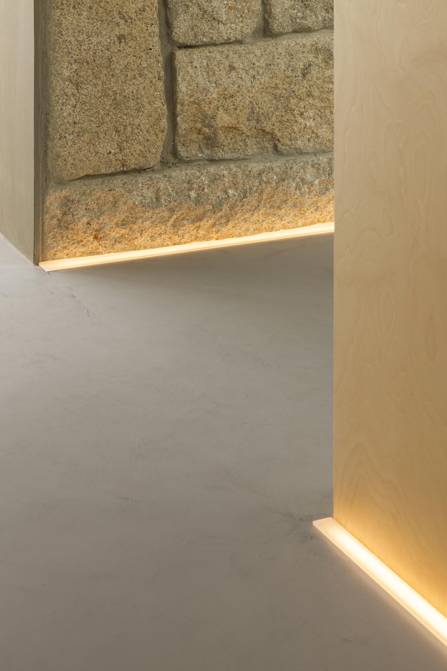 A hallway with stone and wood walls is illuminated by LED lighting on the floor.