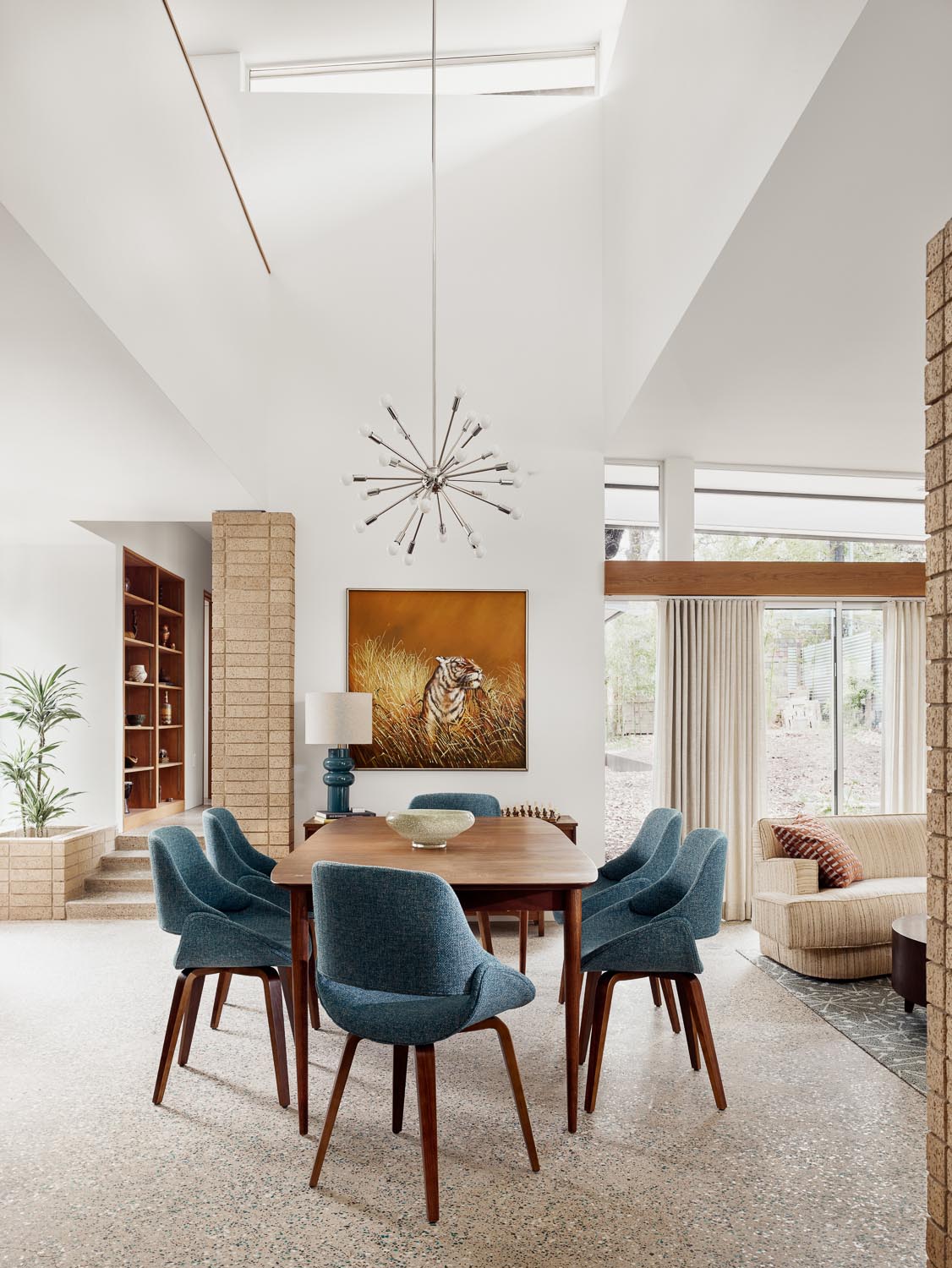 In this mid-century modern inspired dining room, there's a dark wood table with matching chairs that add a pop of color to the open plan interior. A Sputnik inspired pendant light draws the eye upwards to the high ceiling.