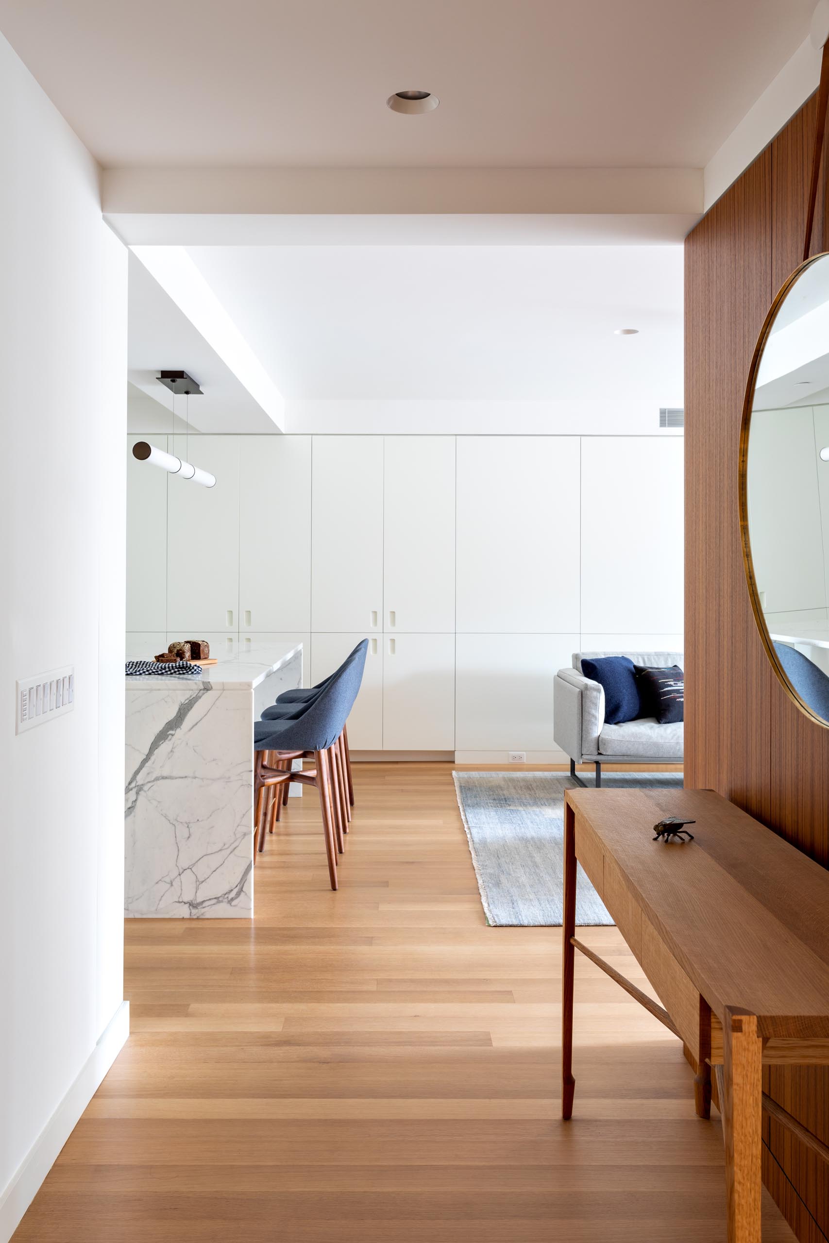 A modern apartment entryway with views of the white kitchen and gray furnished living room.