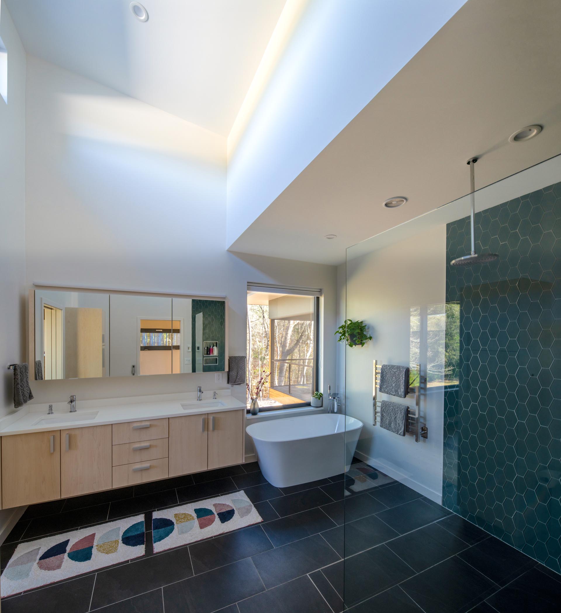 This spa-like master bathroom has high ceiling, black floor tiles, a dual sink vanity, a deep soaking tub, and a shower with a hexagonal tile accent wall.