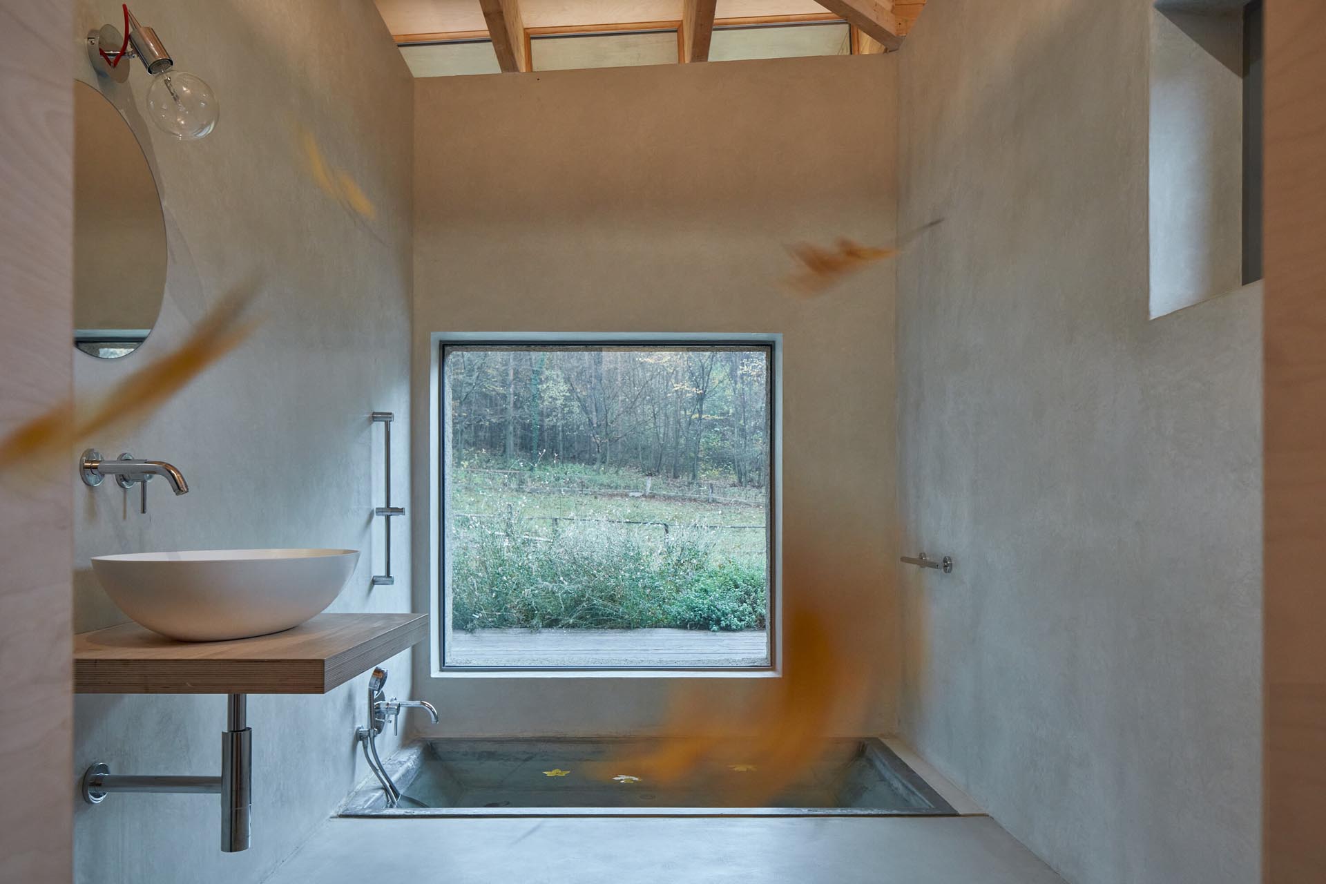 This modern cabin bathroom has been designed with a built-in sunken bathtub, a minimal wood vanity, and a large picture window.