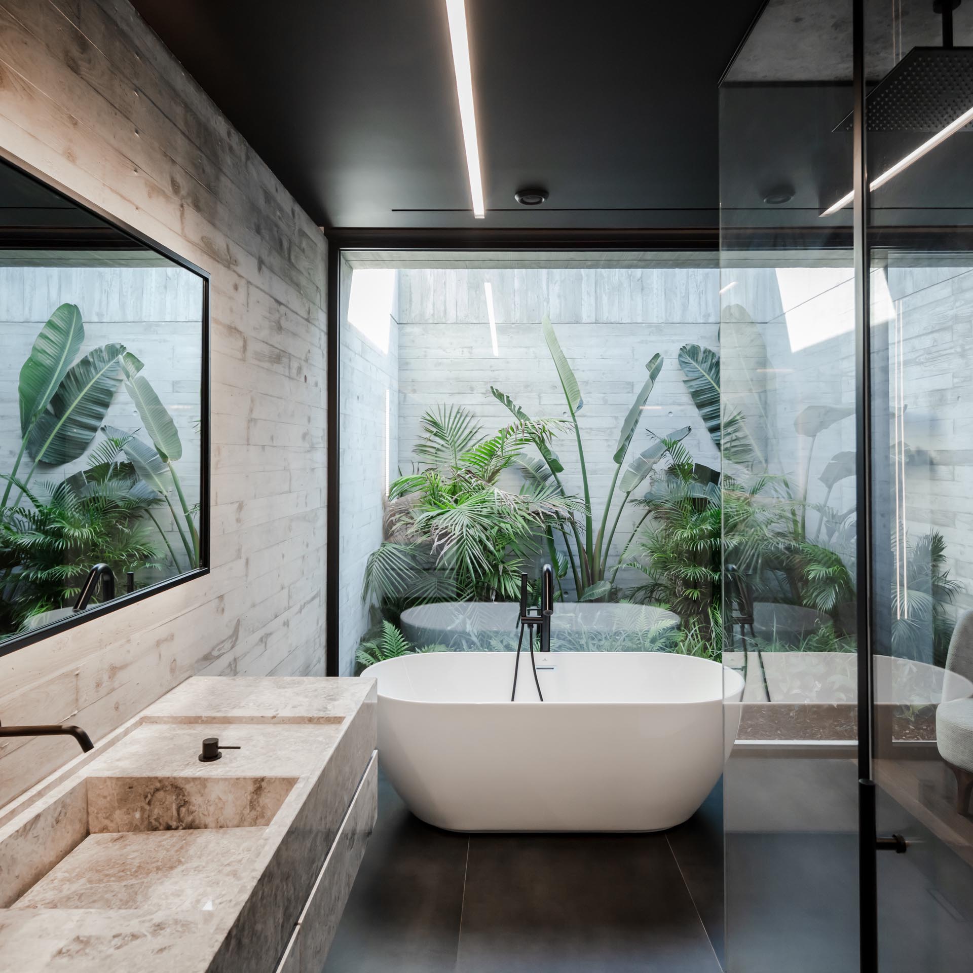 In this modern bathroom, there's a glass wall behind the freestanding bathtub that provides views of a tropical garden.