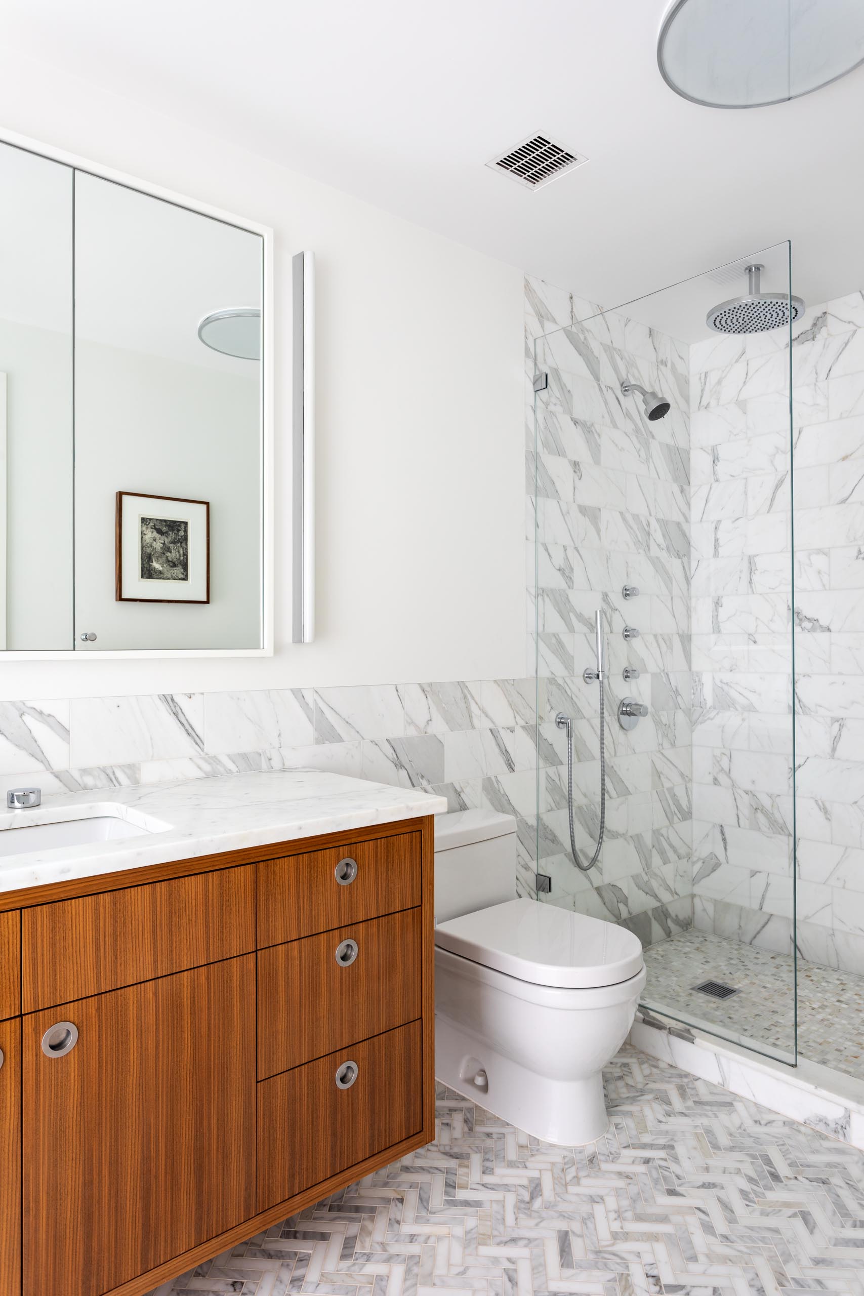 In this mdoern bathroom, there's a floating wood vanity with a tri-panel mirror mounted to the wall, and a marble backsplash that continues through to the shower.