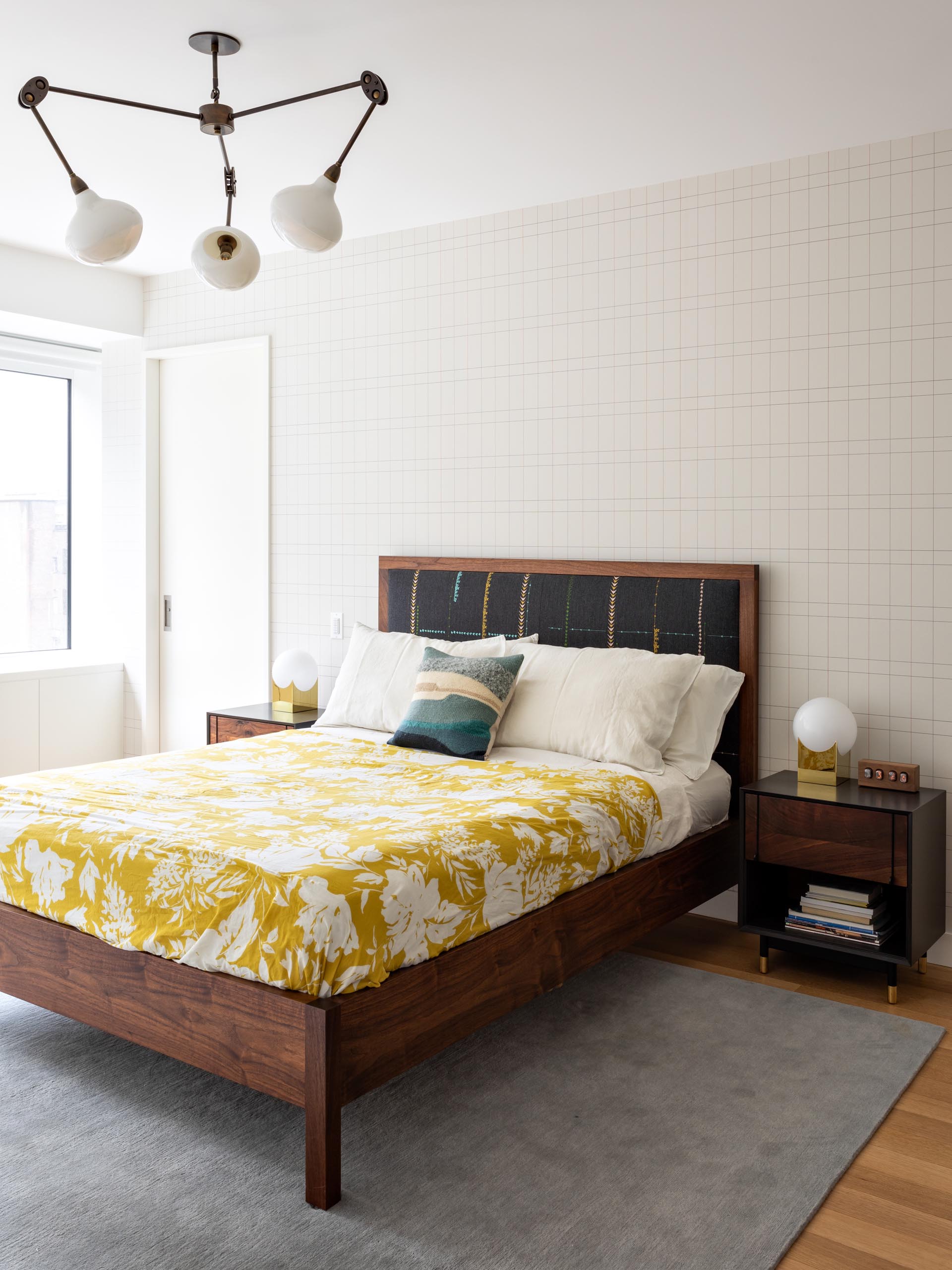 A modern master bedroom that includes wood furniture, pops of color, and a graphic accent wall.