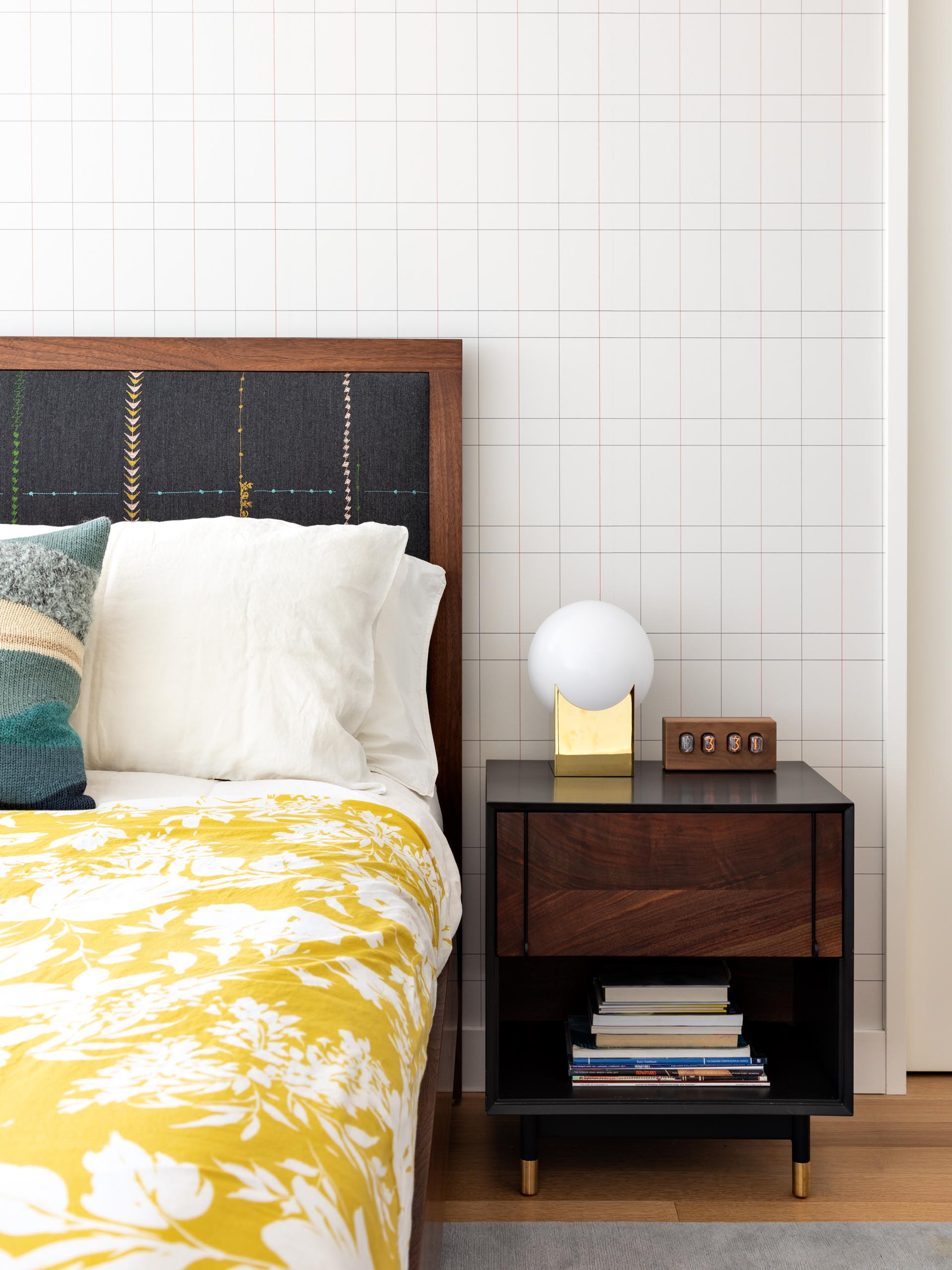 A modern master bedroom that includes wood furniture, pops of color, and a graphic accent wall.